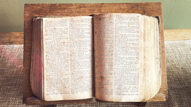 An open, aged book rests on a wooden stand.