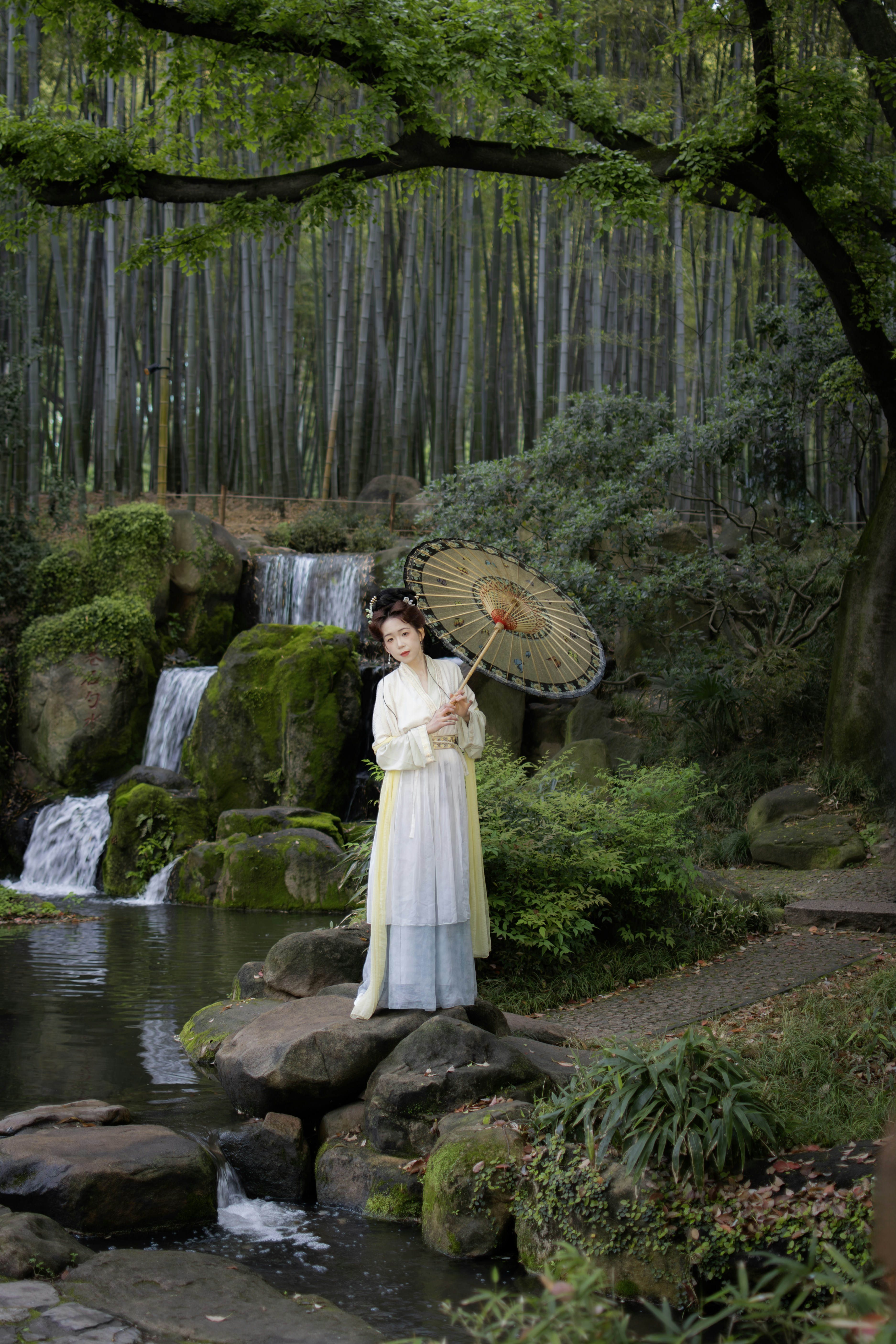 Femme en tenue traditionnelle tient un parapluie près de la cascade