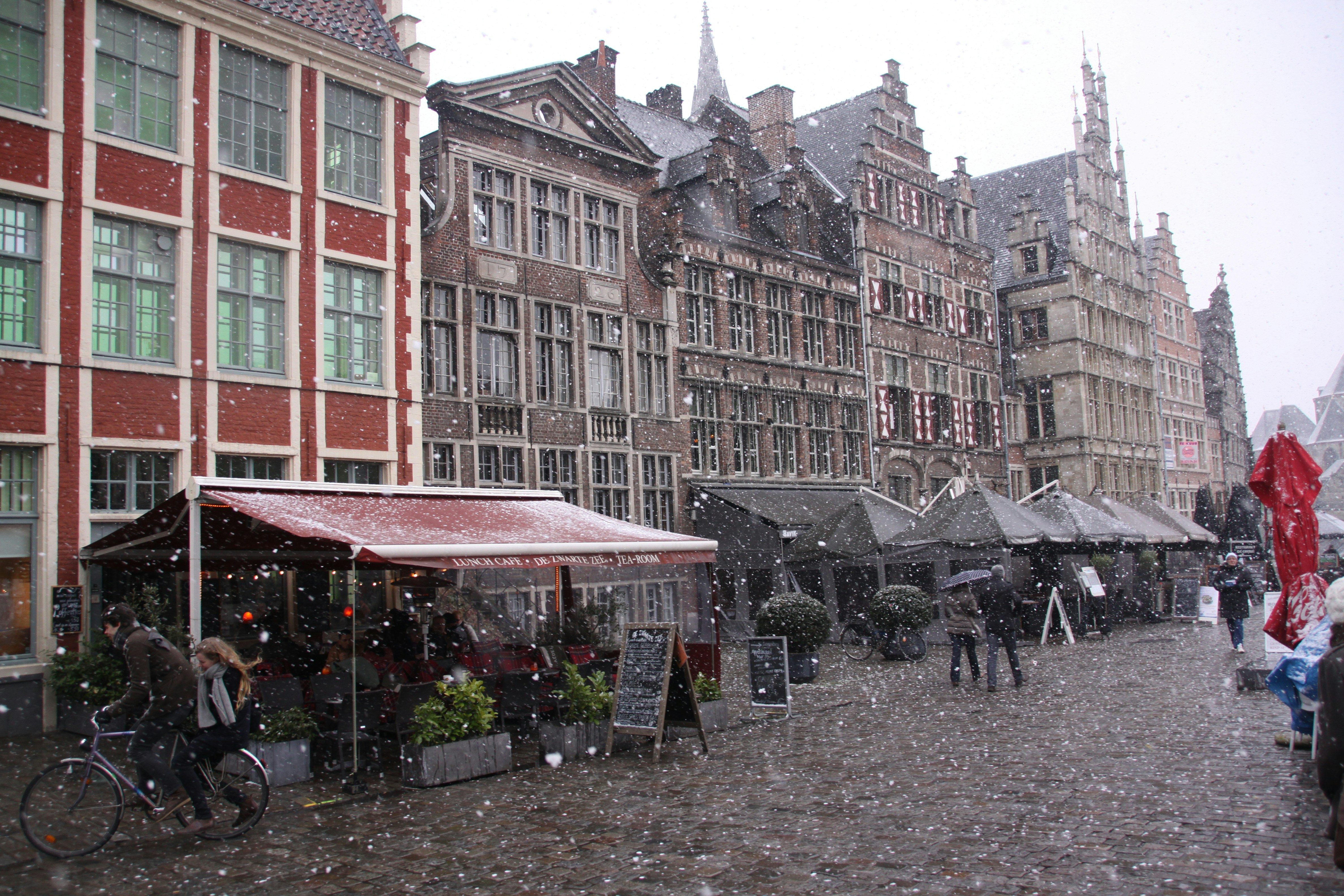 Snow falls on a european city street with historic buildings.