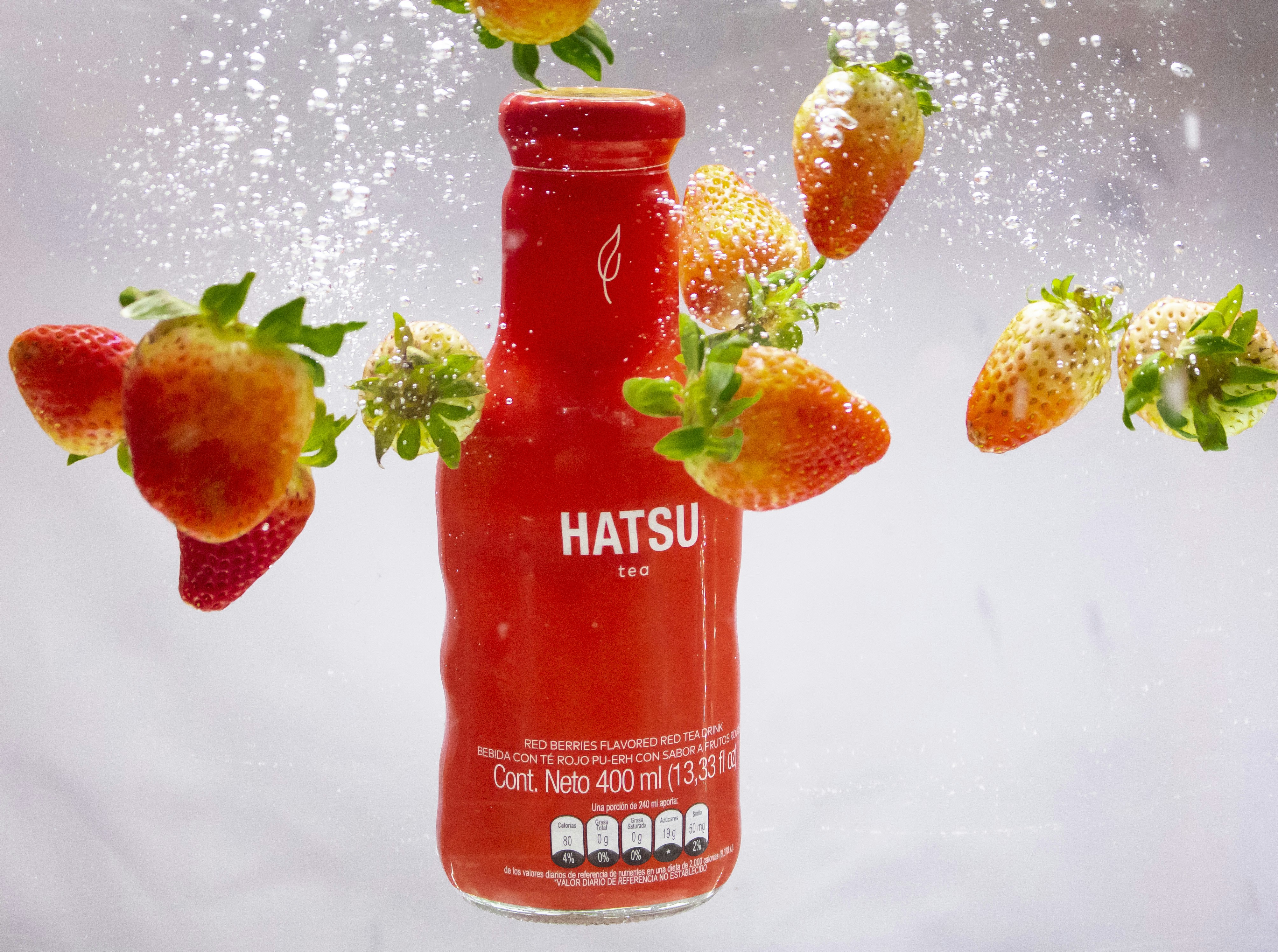 Red bottle of hatsu drink surrounded by strawberries