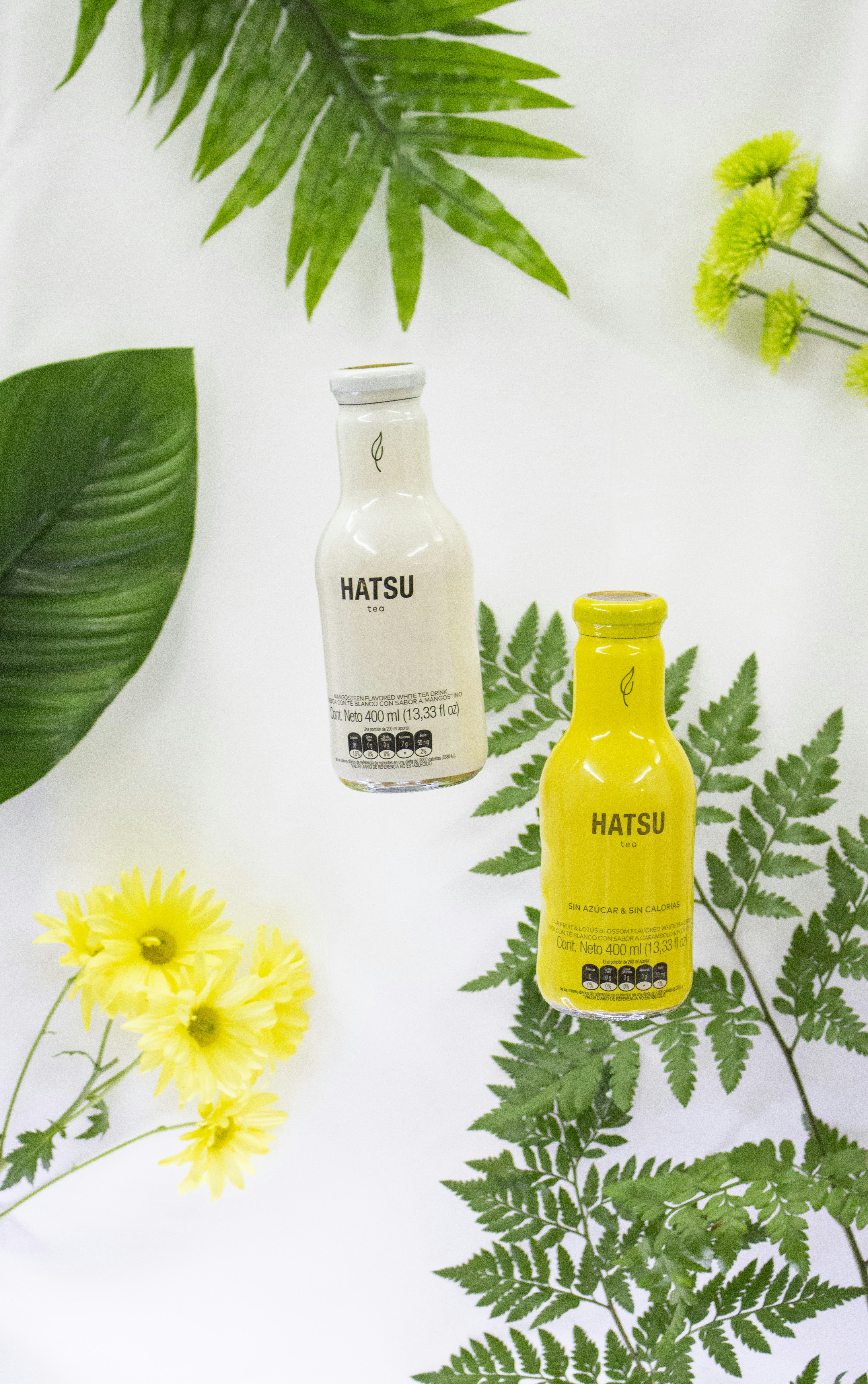 Two bottles of hatsu drink surrounded by leaves and flowers
