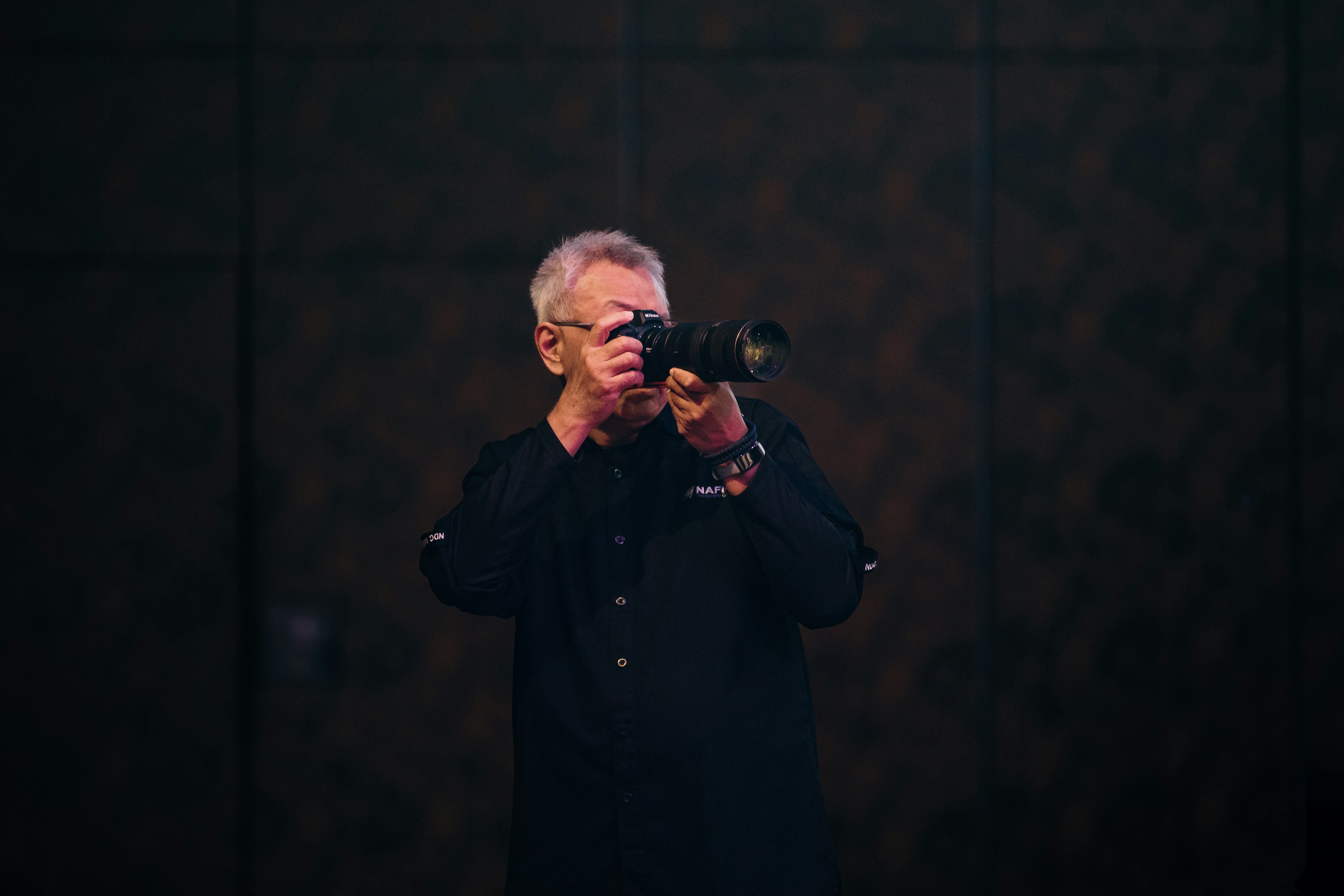 Man with glasses holding a camera and taking a picture.