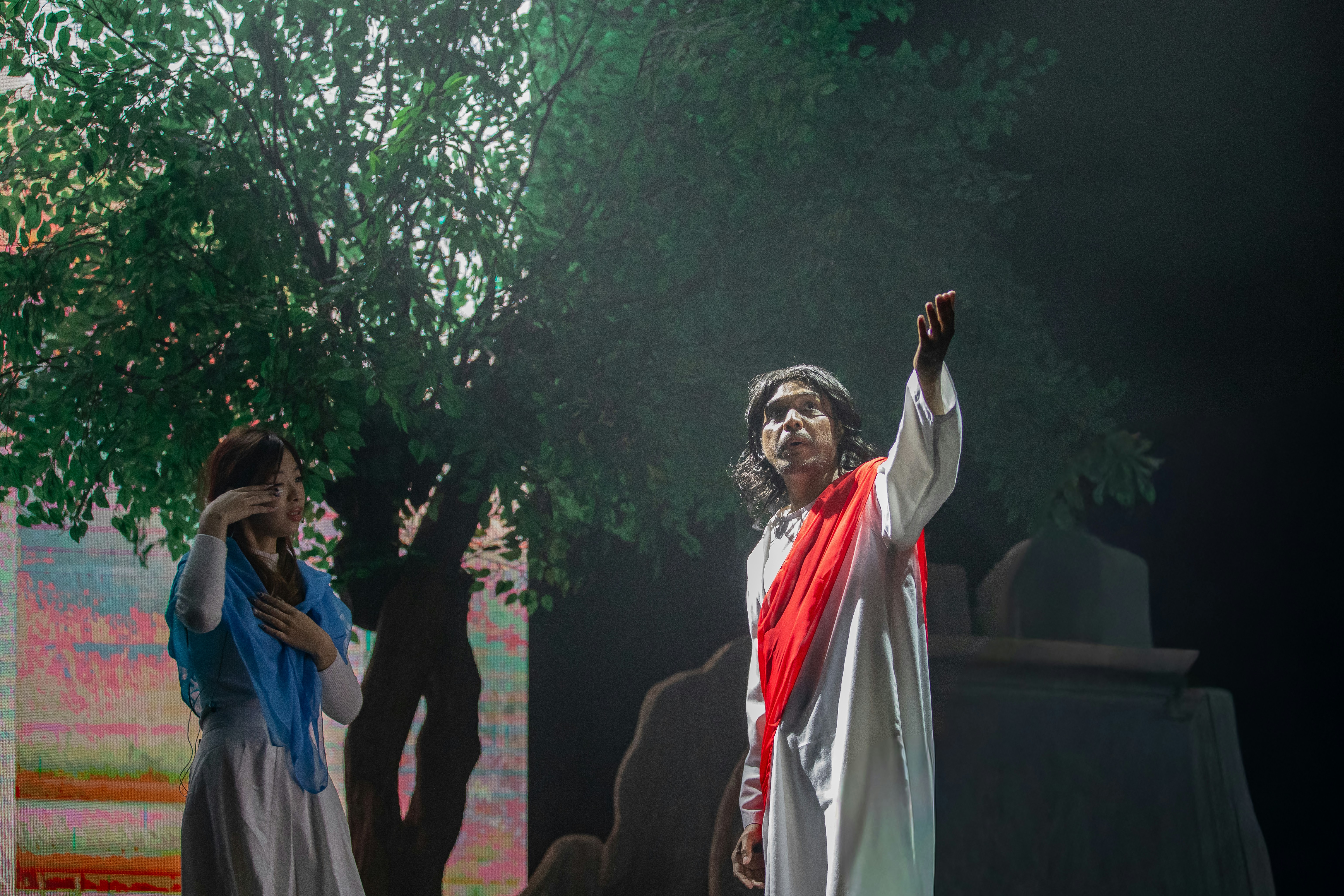 Two actors perform on a stage with a tree backdrop