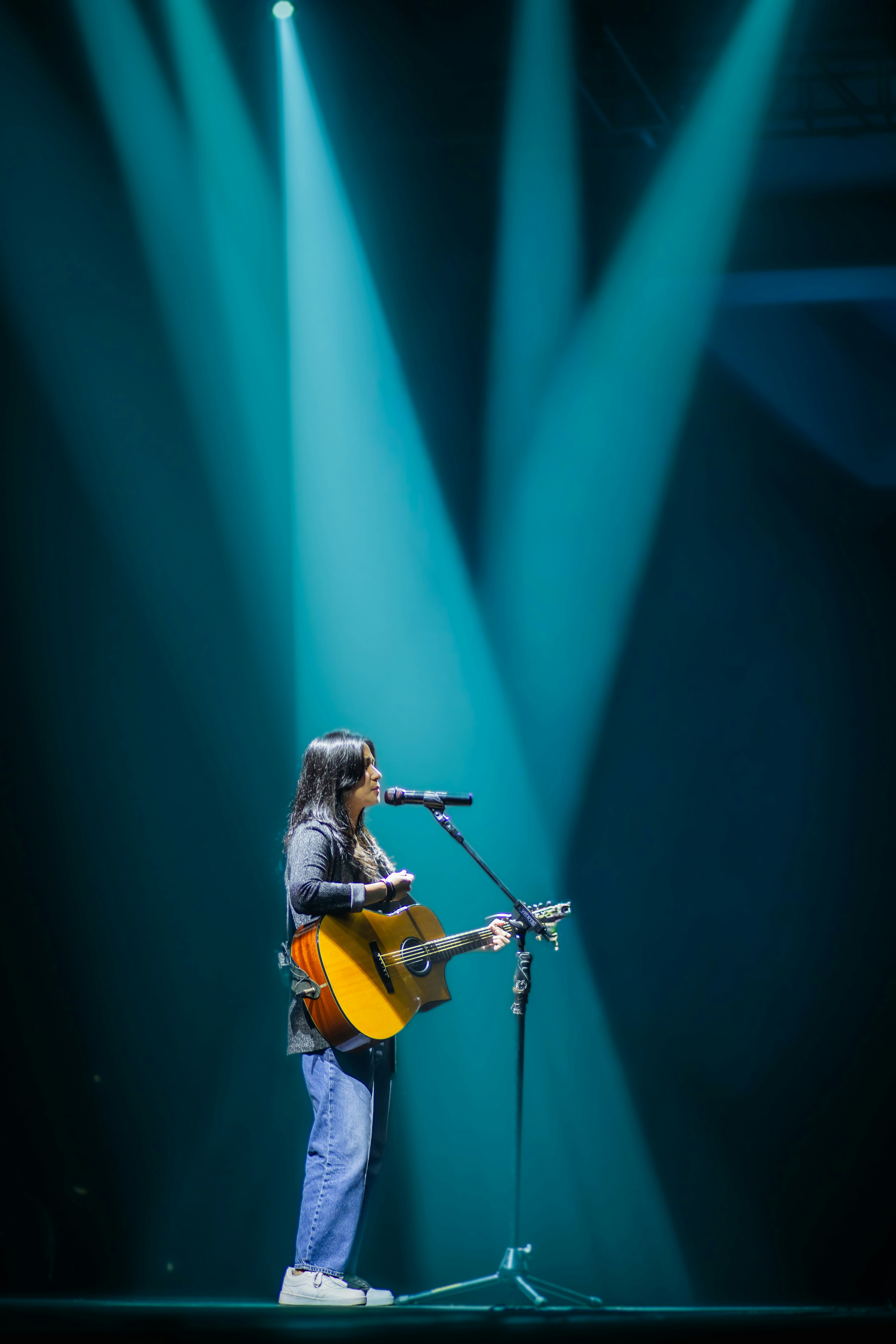 Una mujer canta y toca la guitarra en un escenario oscuro.
