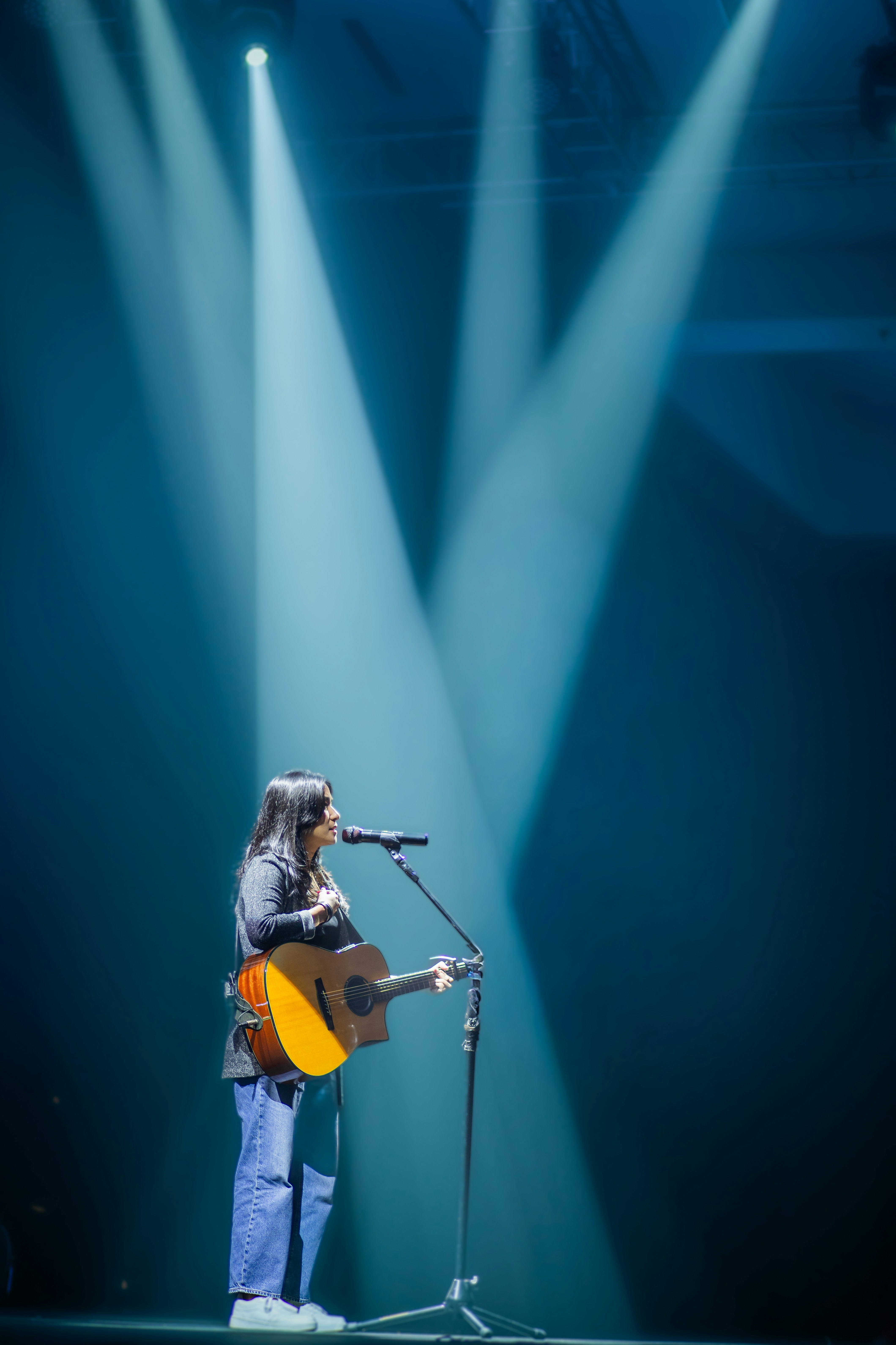 Wanita bernyanyi dan bermain gitar di atas panggung dengan lampu sorot