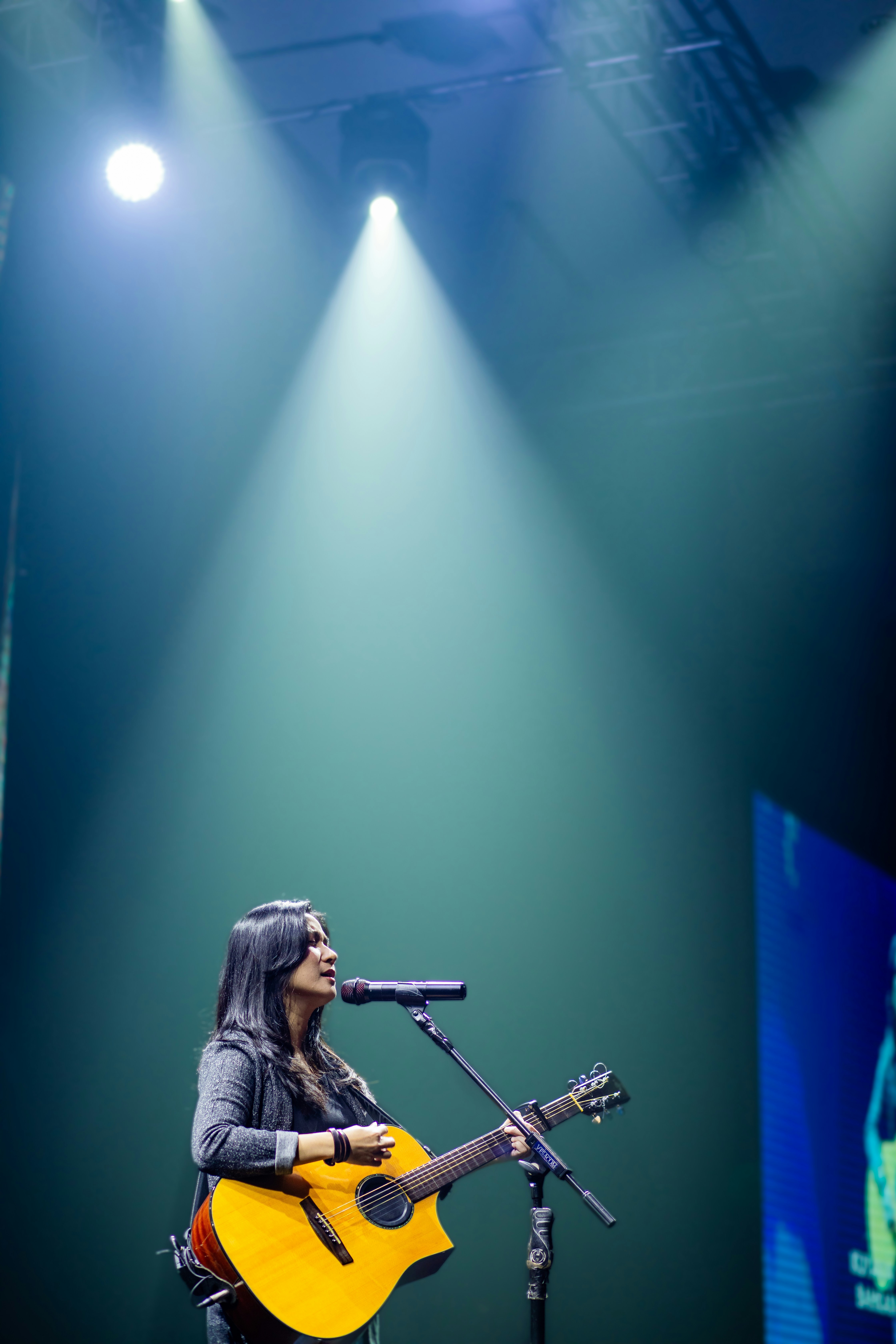 Seorang wanita bernyanyi dan bermain gitar di atas panggung.