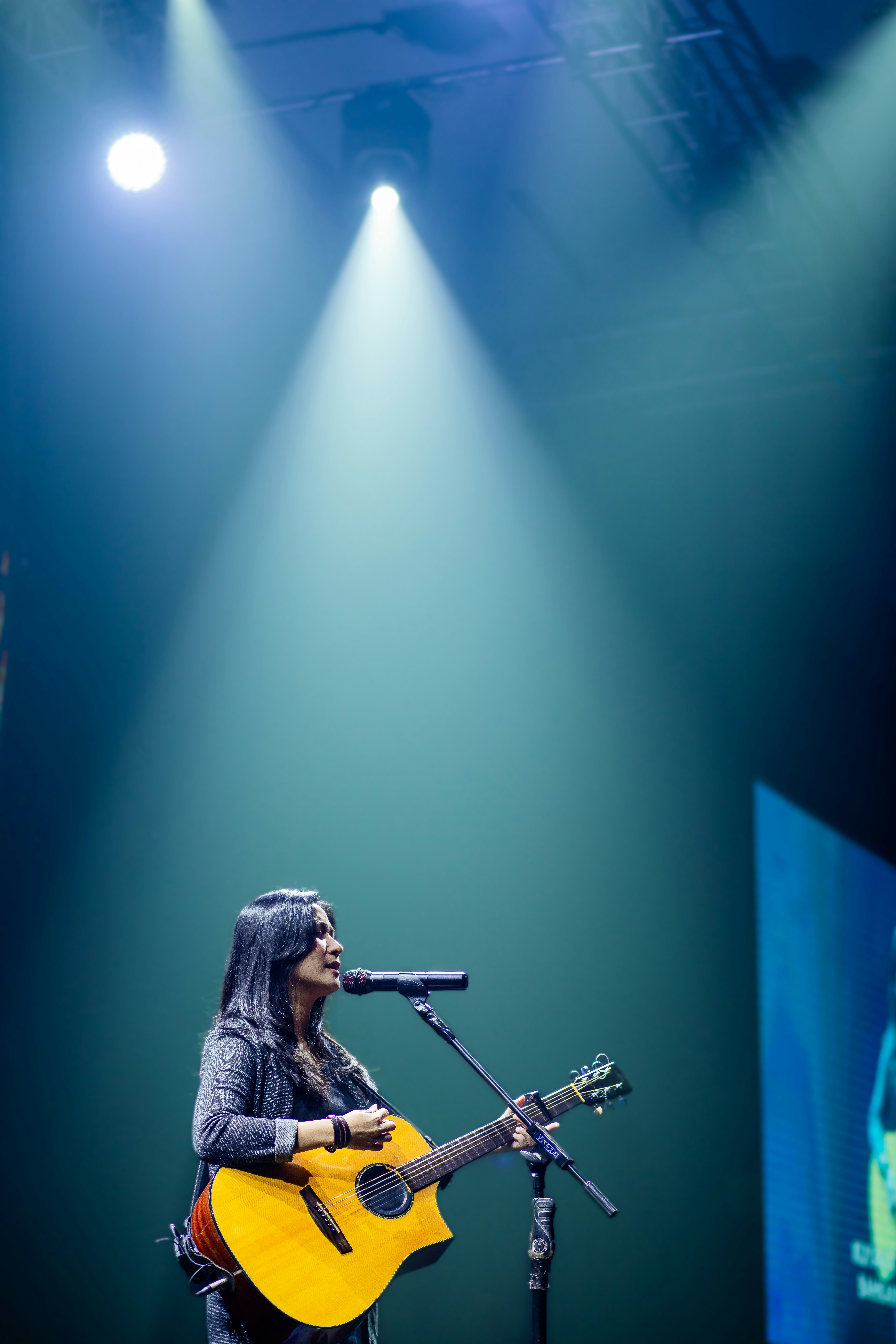 A woman sings into a microphone while holding a guitar.