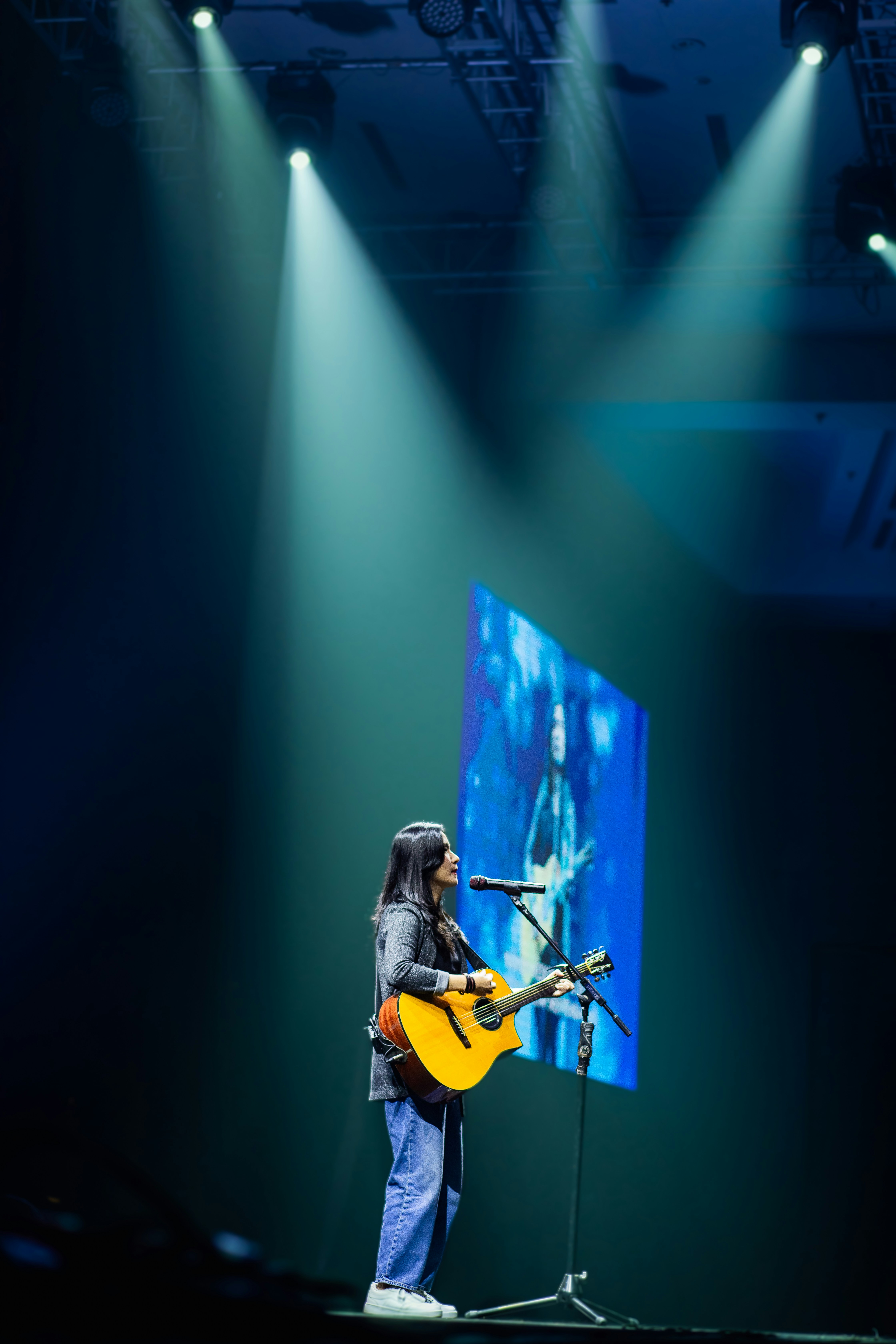 Mujer tocando la guitarra en el escenario con focos y pantalla