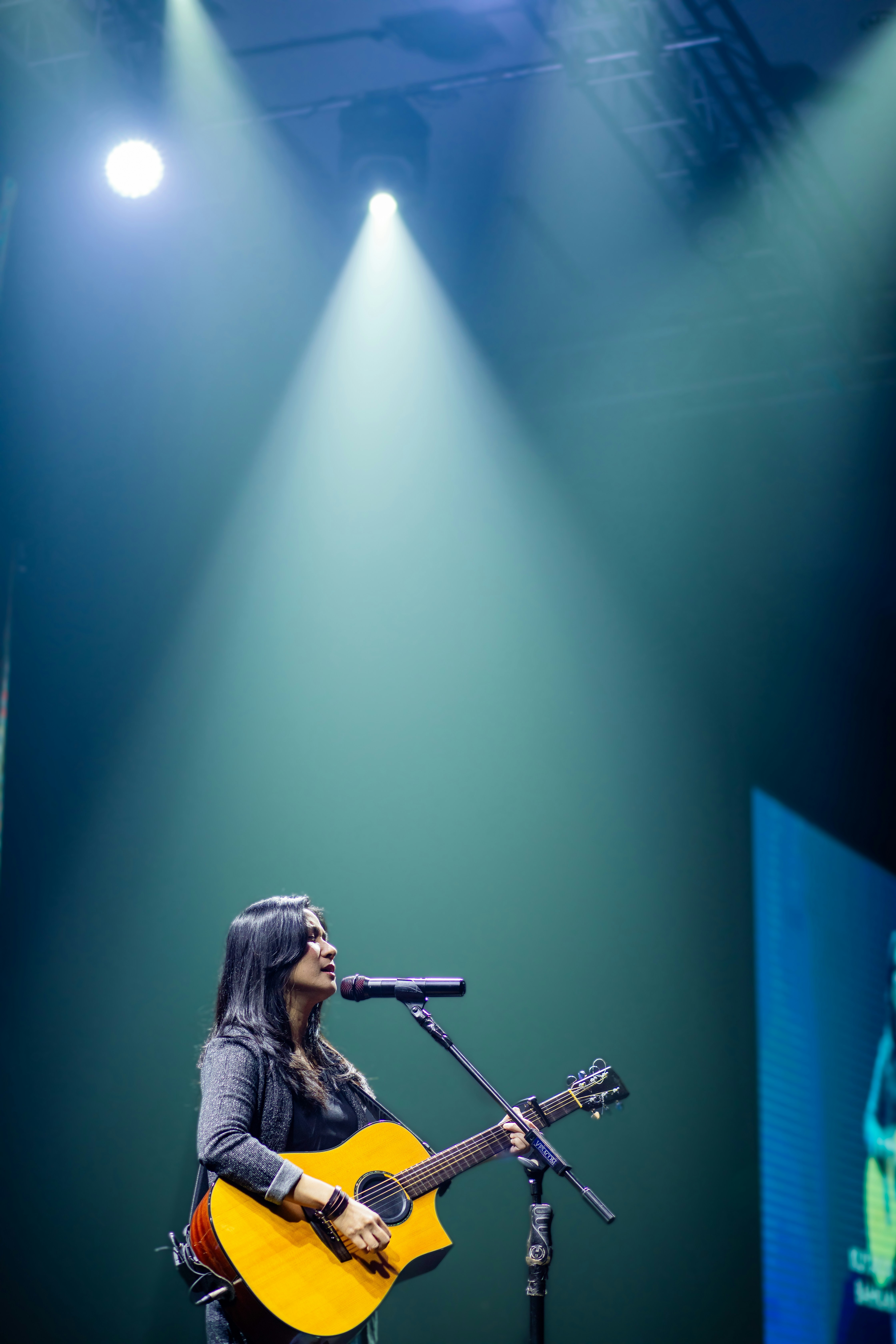 Wanita bermain gitar dan bernyanyi di atas panggung.