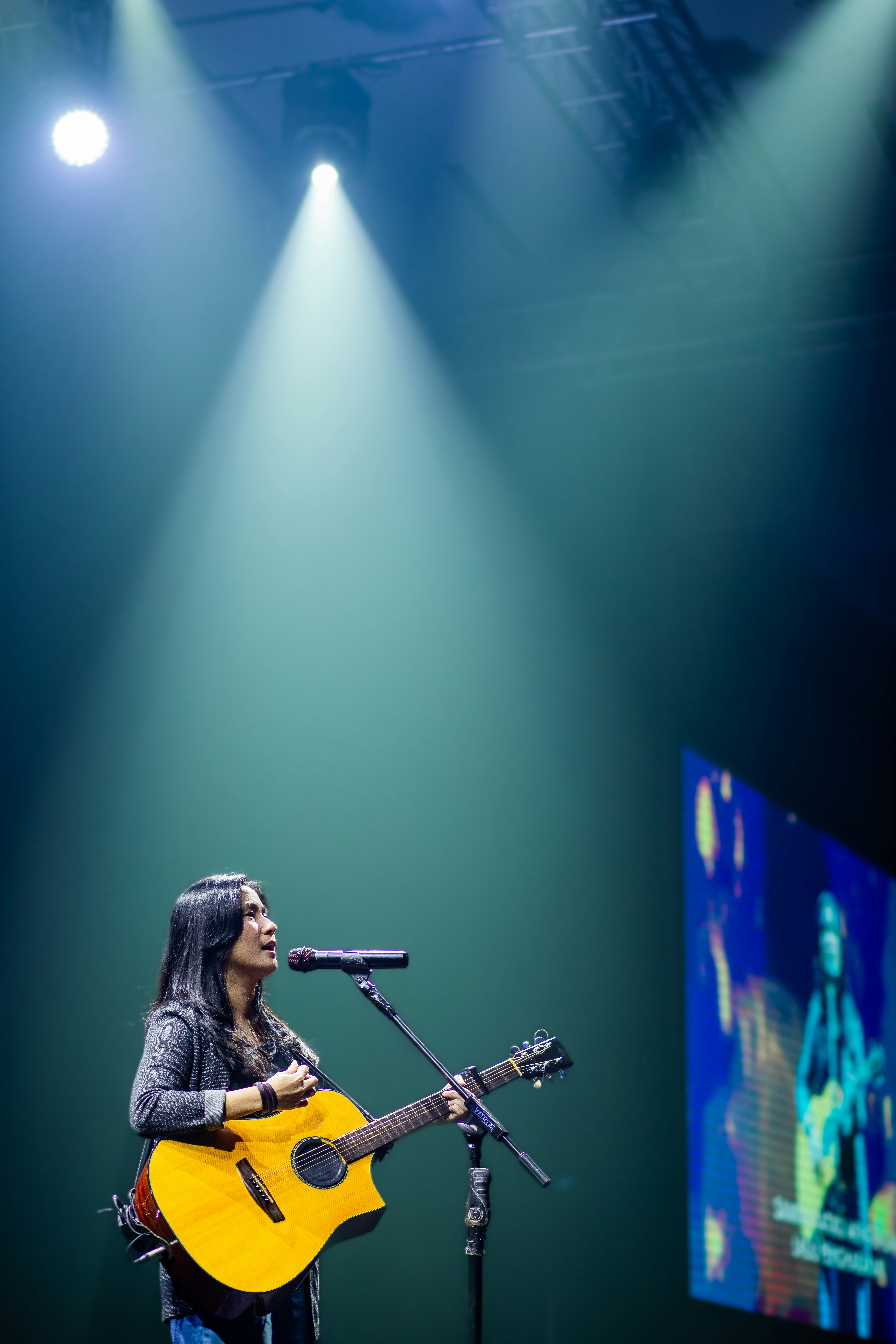 Seorang wanita bermain gitar dan bernyanyi di atas panggung.