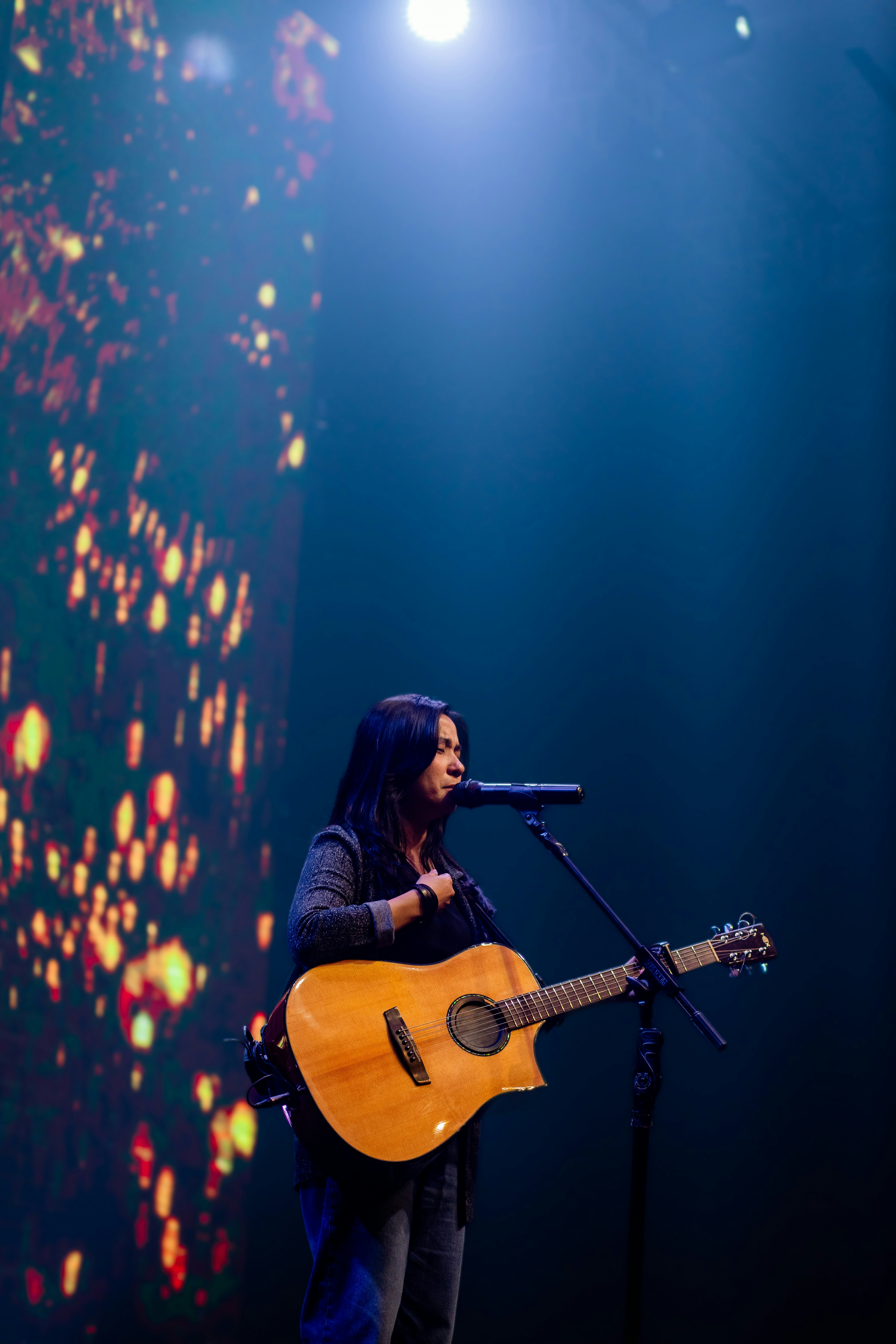Seorang wanita bernyanyi ke mikrofon sambil bermain gitar.