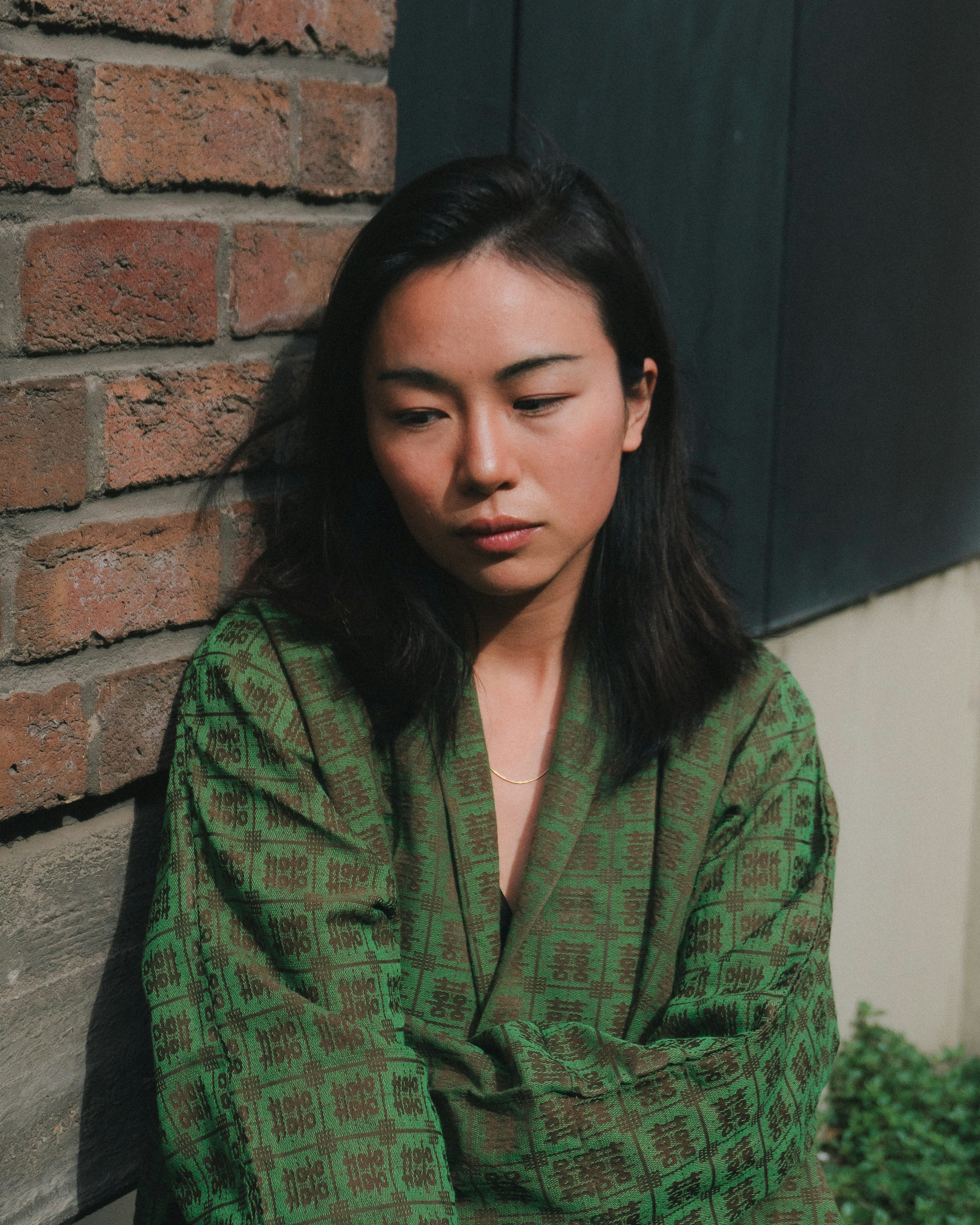 Young woman in green robe leans against brick wall