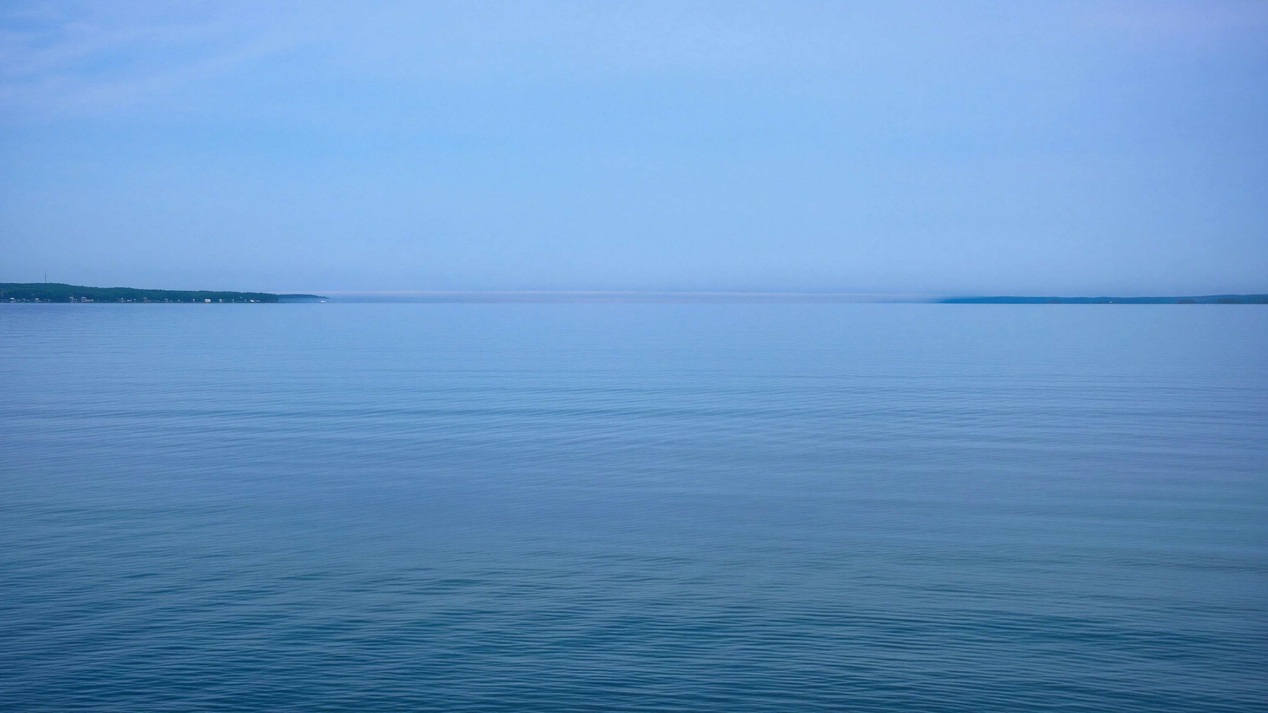 Lago azzurro calmo con terra lontana all'orizzonte