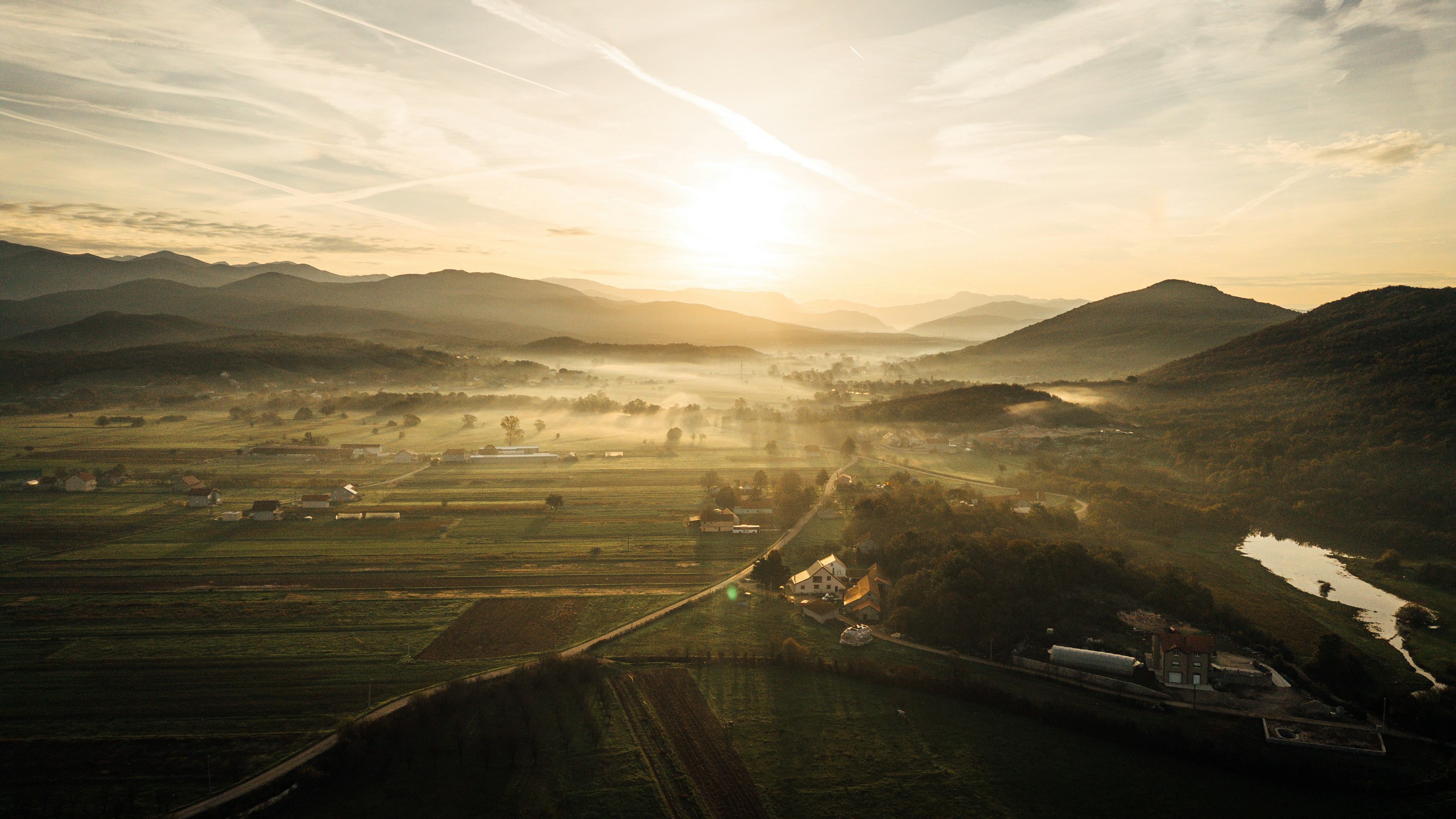 Amanecer sobre un valle brumoso con colinas onduladas.