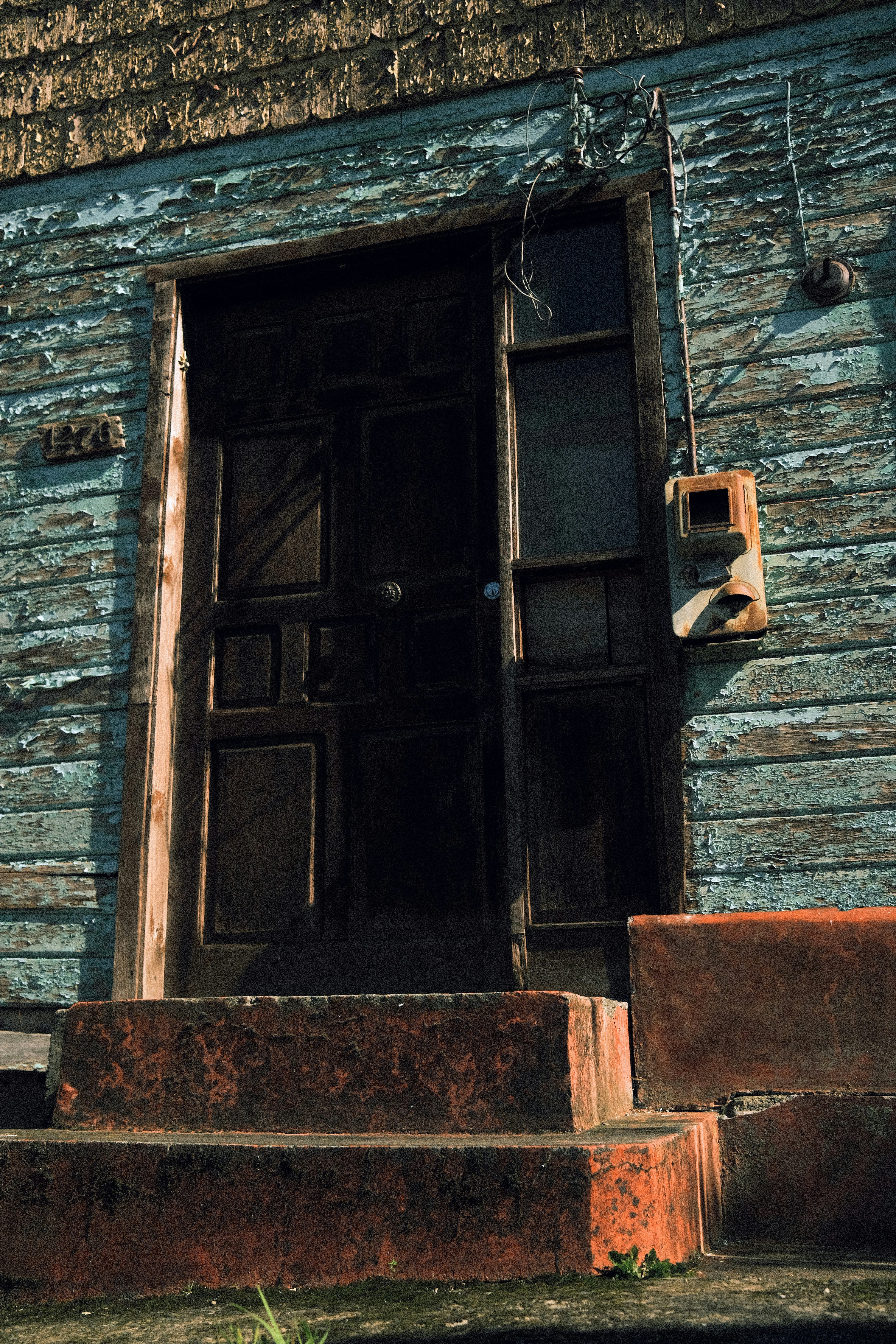 Rumah biru lapuk dengan pintu kayu gelap.