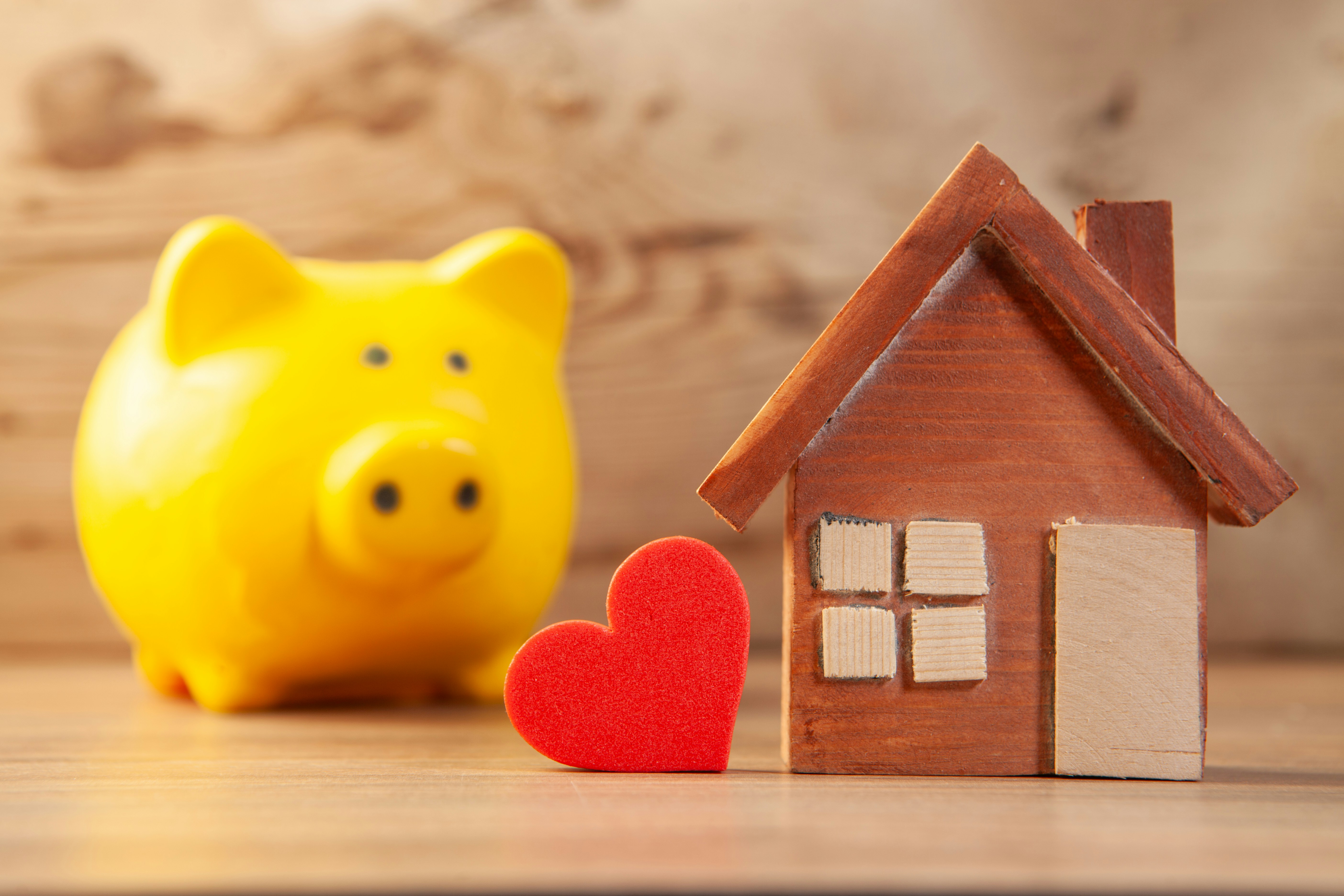 House, piggy bank and red heart on wooden background. Mortgage concept