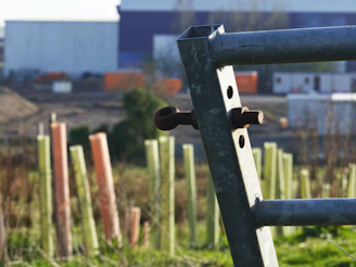 Metal fence post with protective tree guards in background.