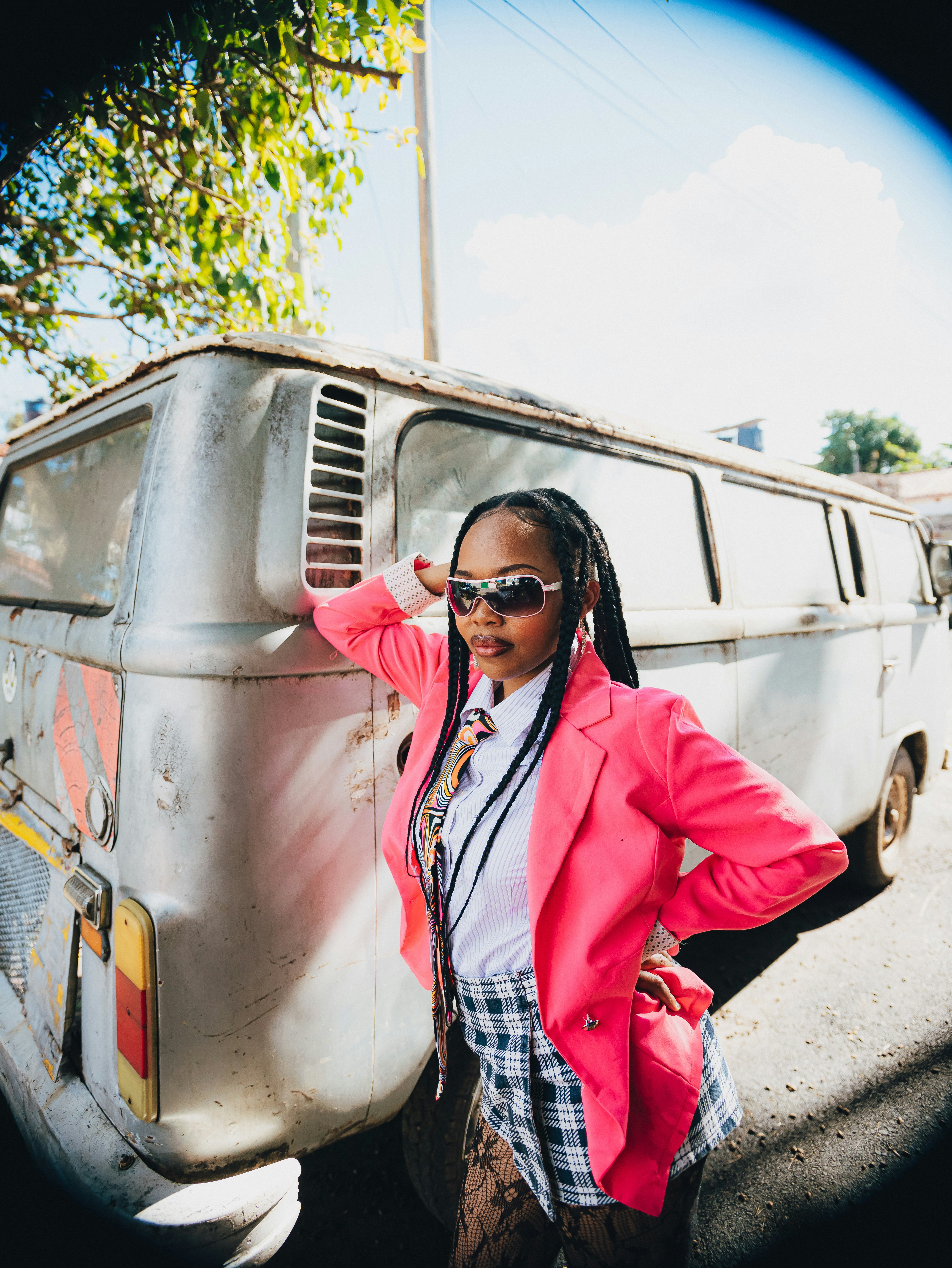 Woman in pink blazer and plaid skirt poses by van.