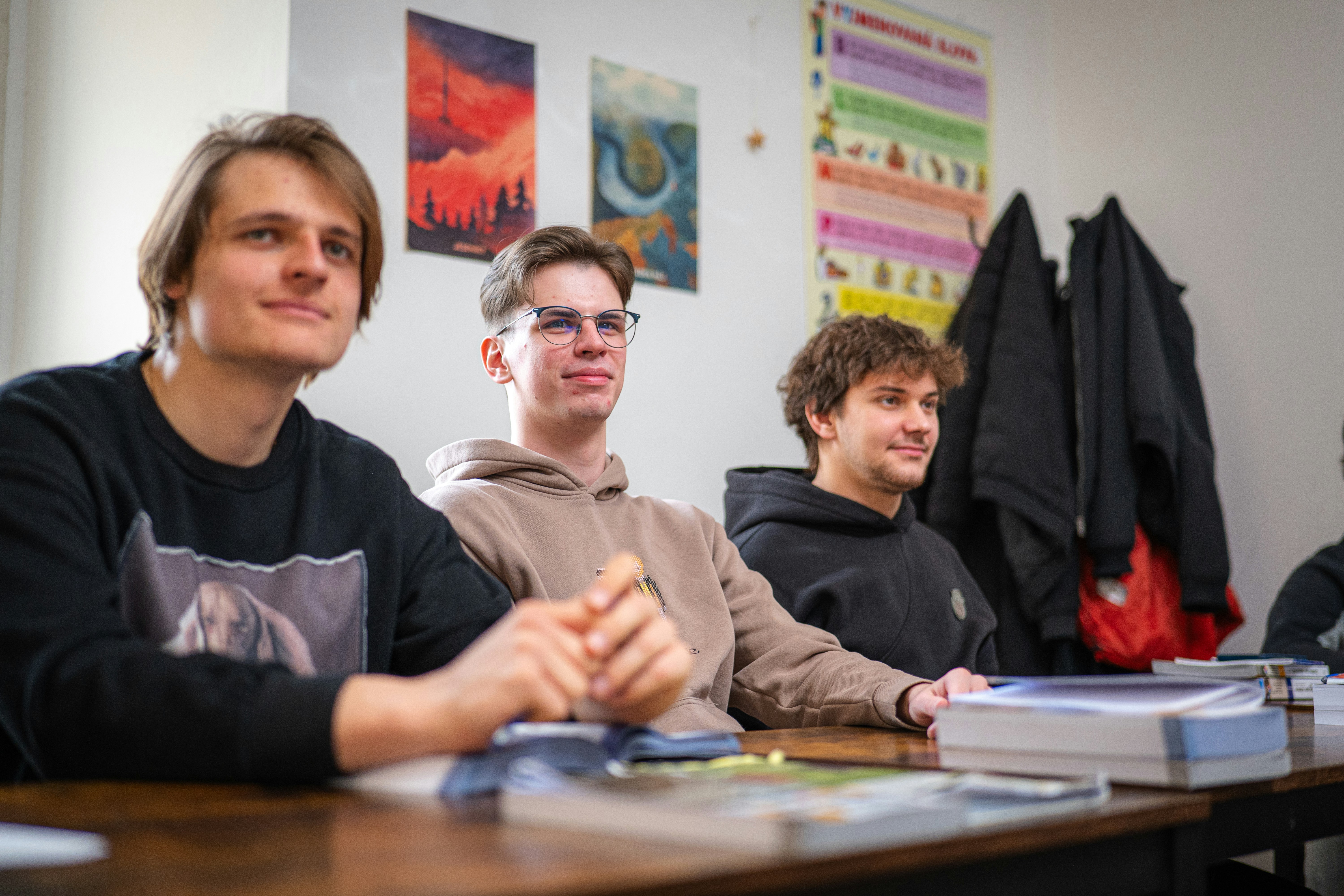 Three young men sitting at a table in a classroom.