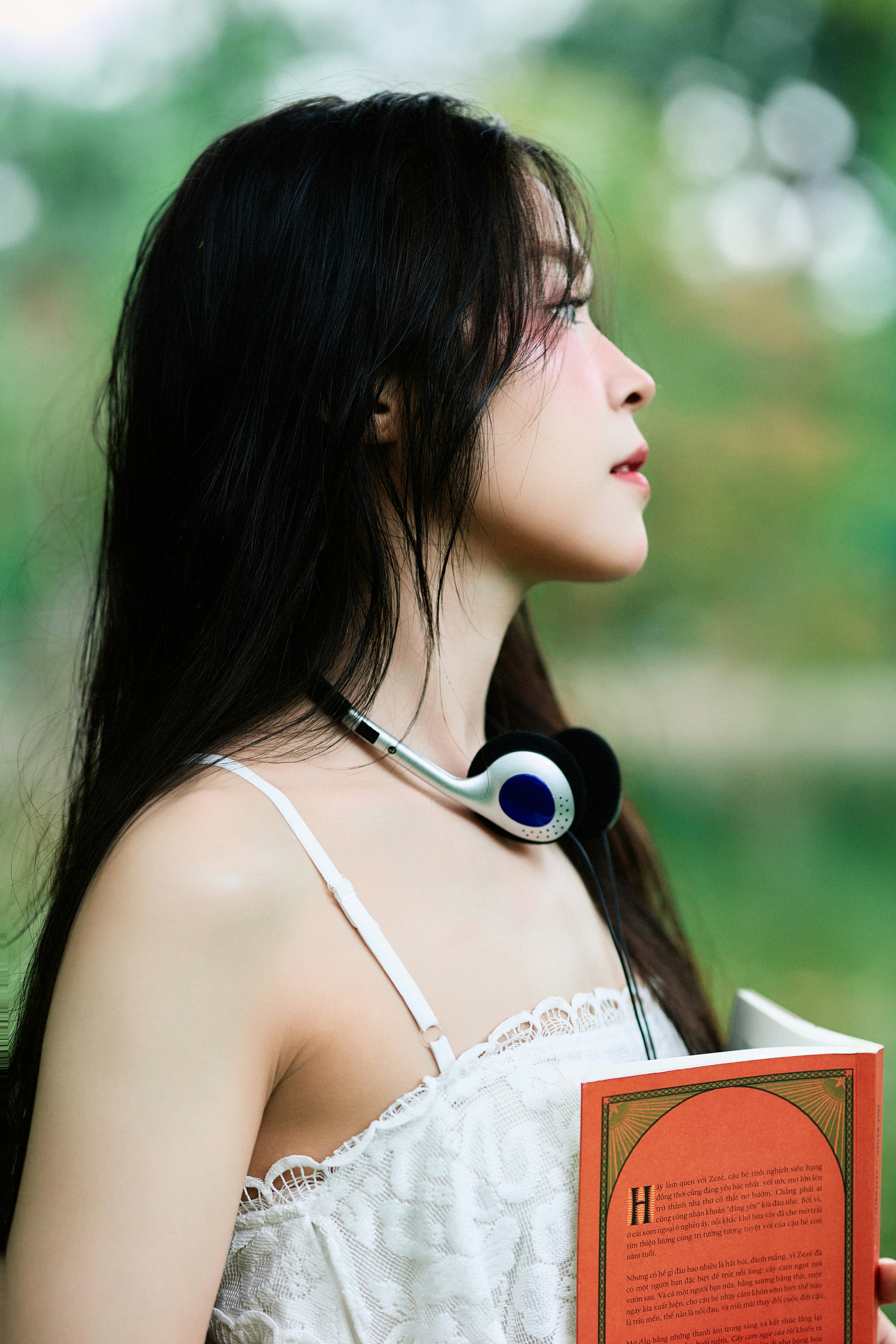 Young woman with headphones holds a book outdoors.