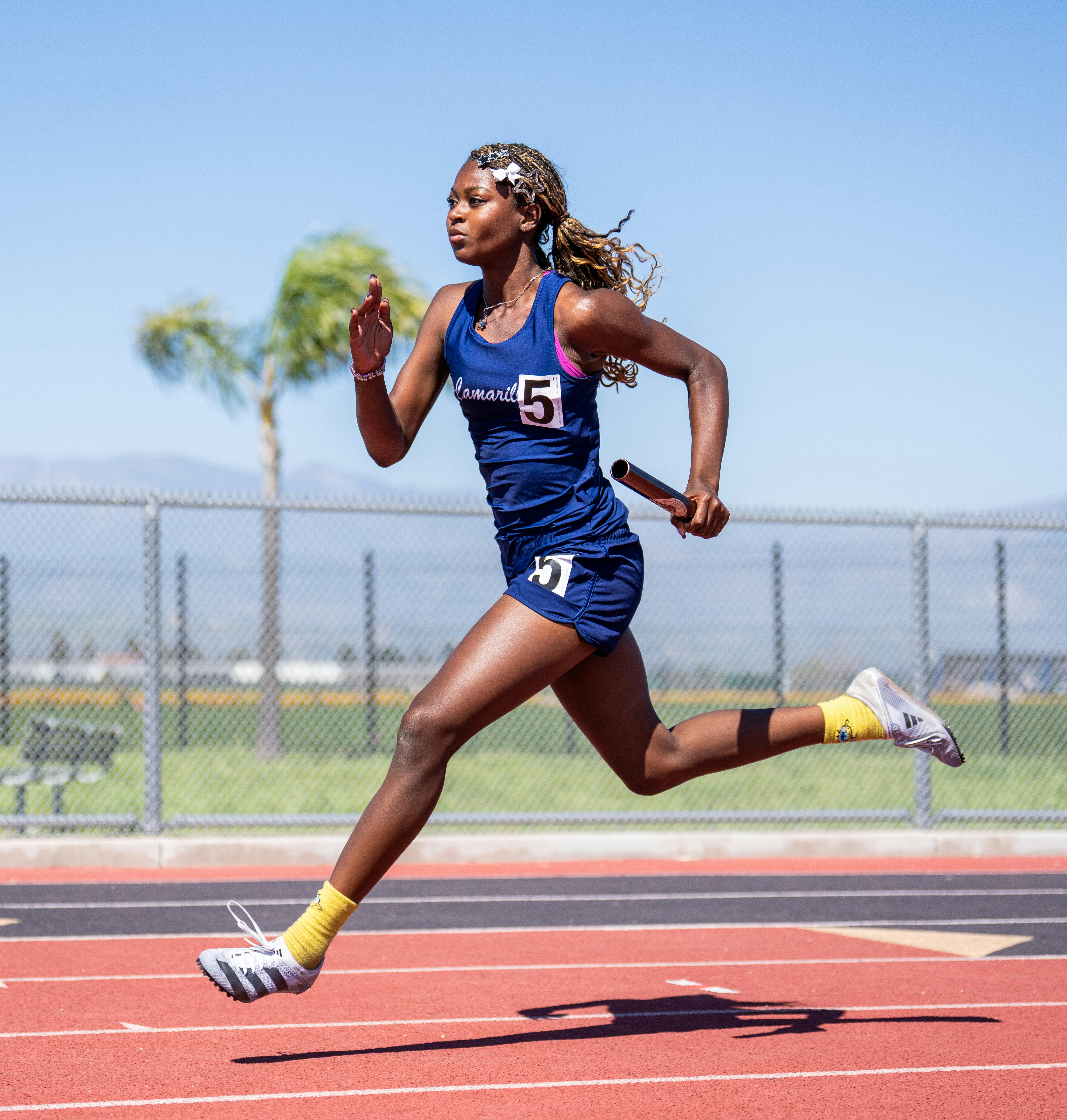 A female runner sprints on a track holding a baton.