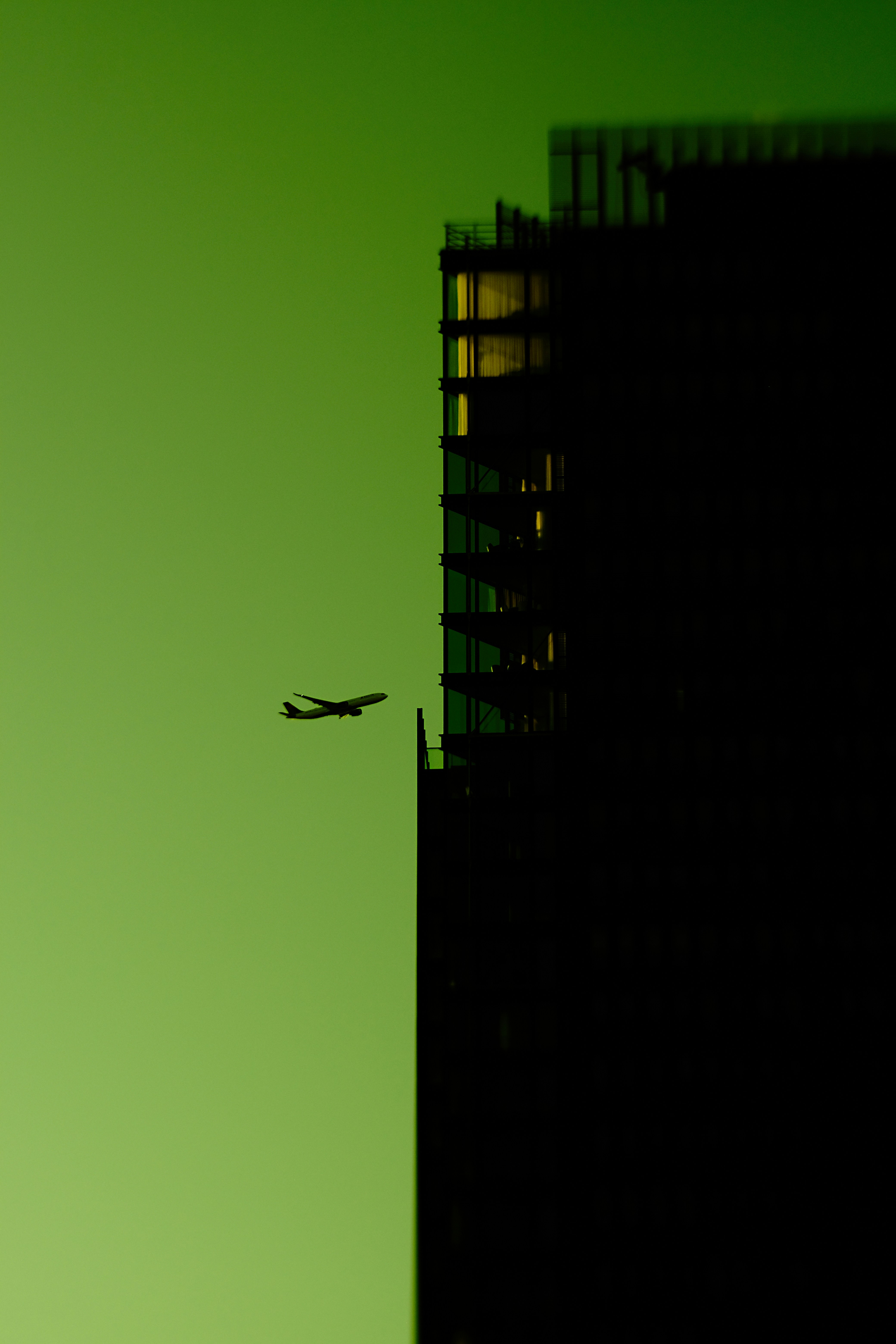 Airplane flying past a silhouetted building at dusk.