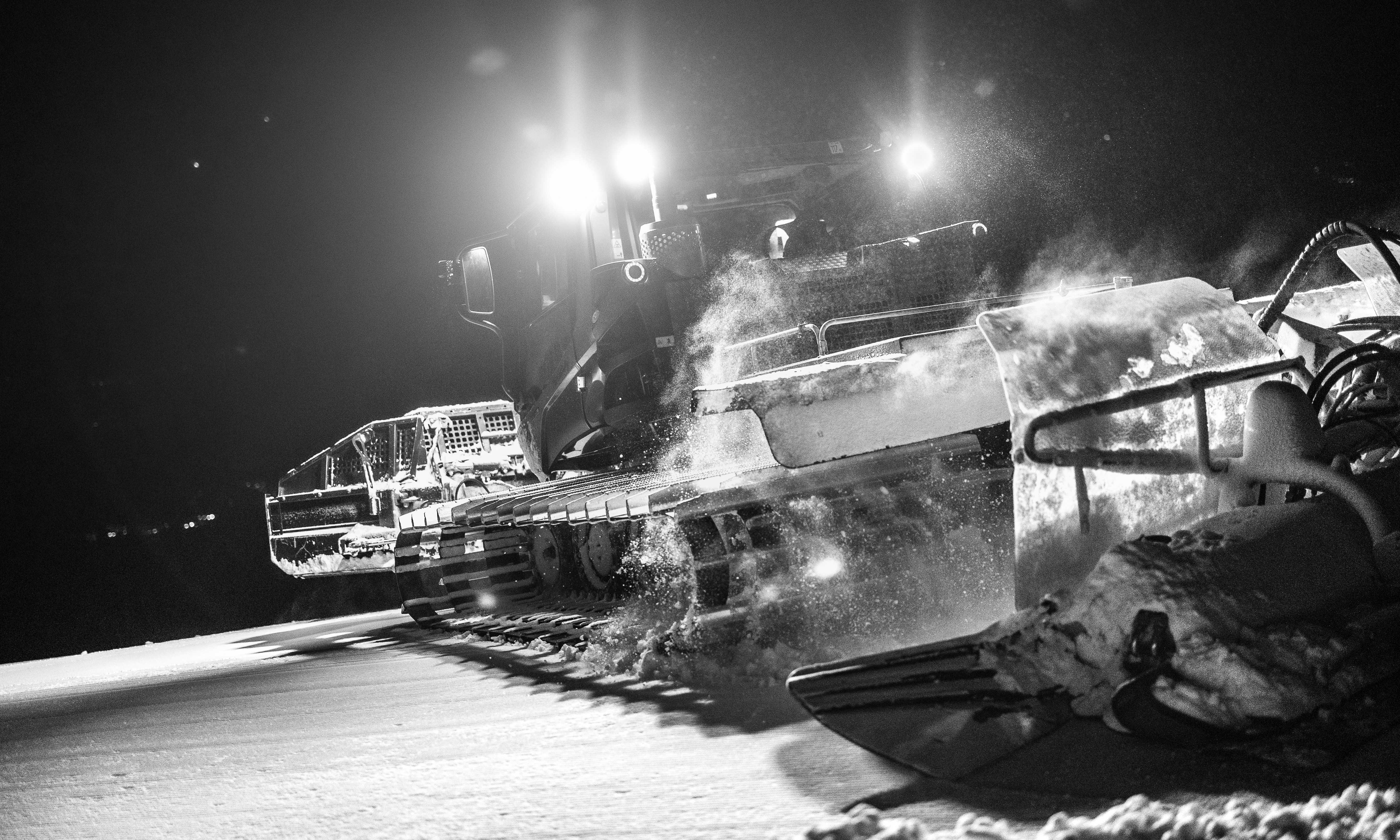 Snow groomer working on a slope at night.