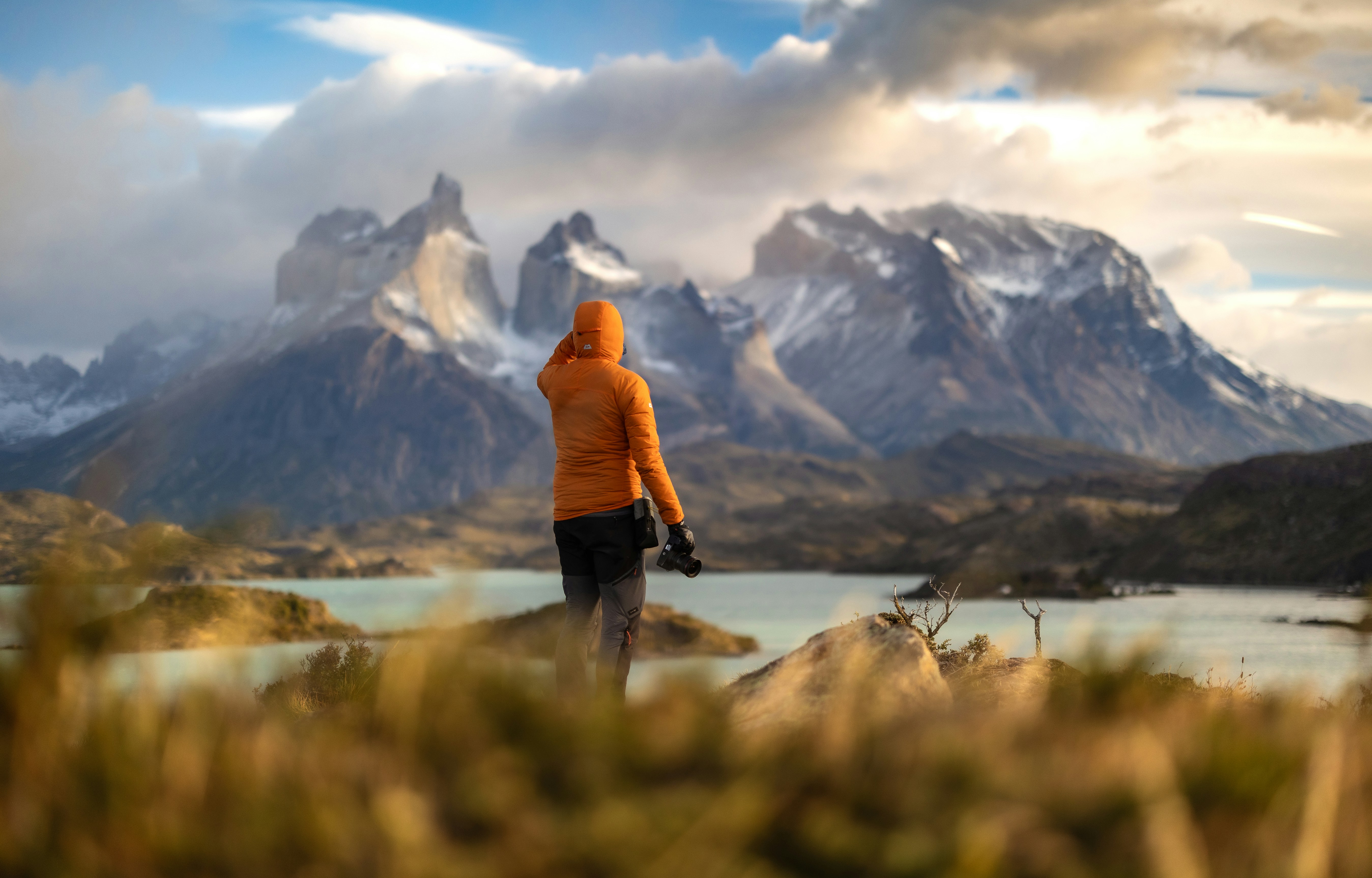 Person in orange jacket overlooks snowy mountains and lake