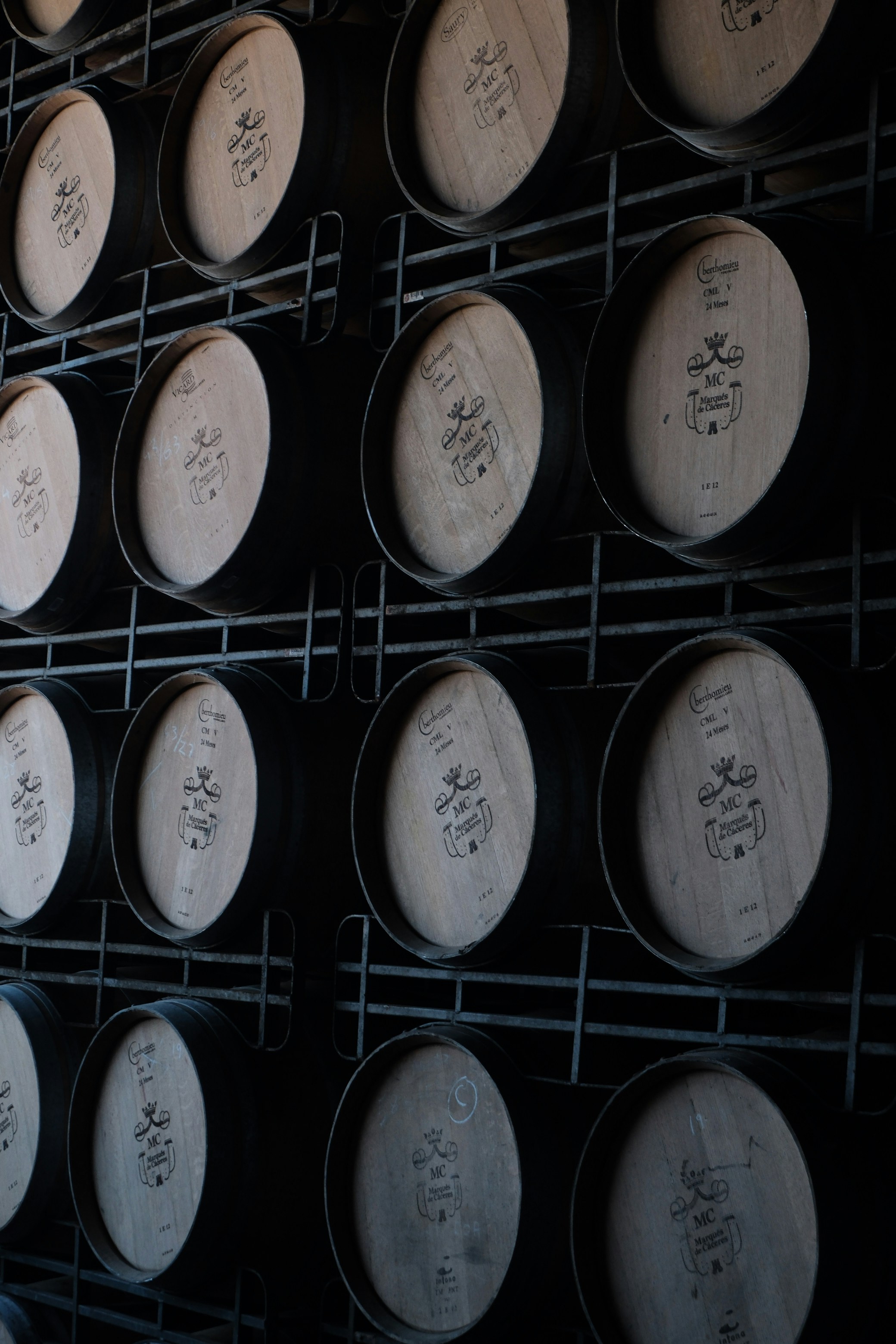 Wooden barrels stacked on metal racks in a cellar.