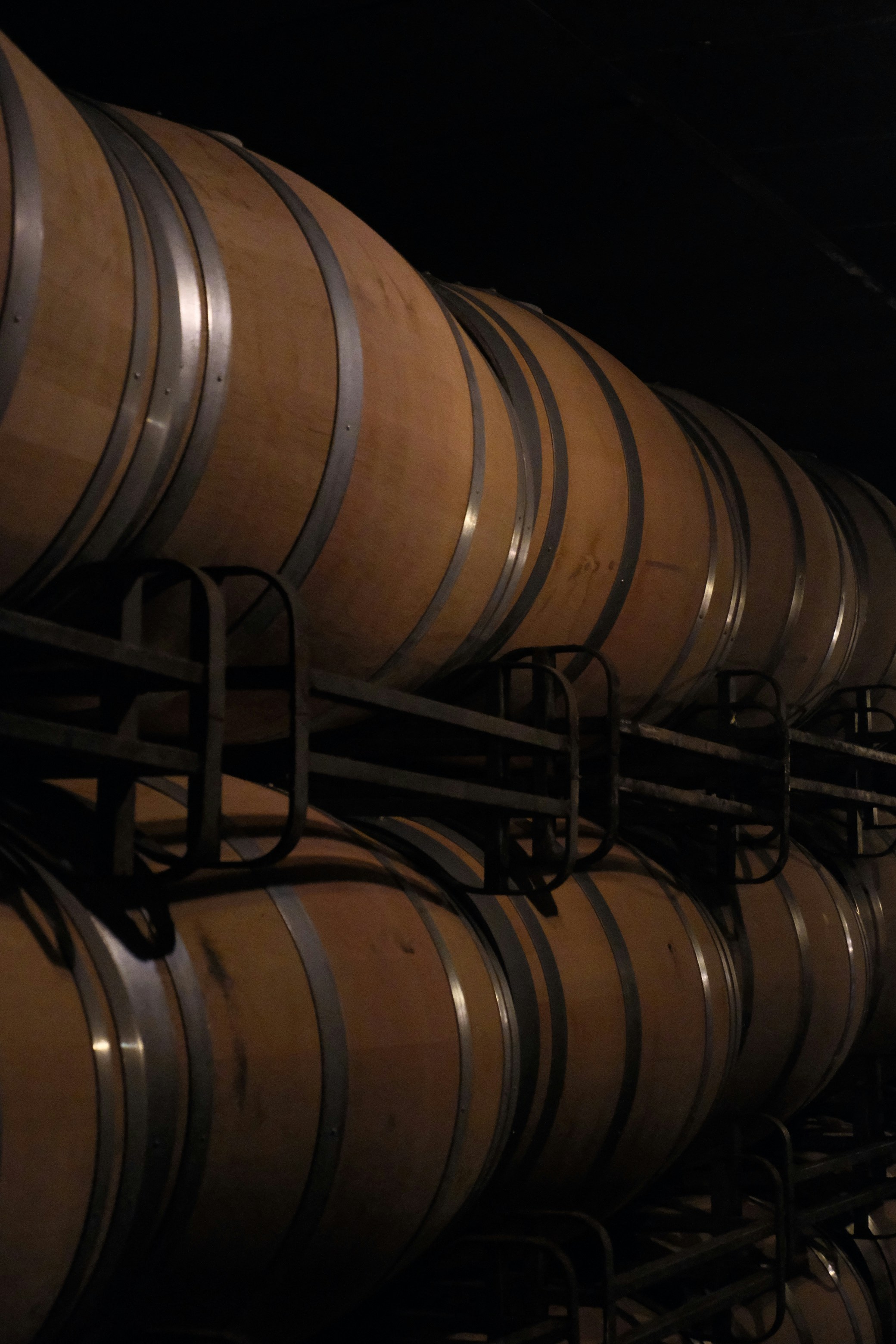 Filas de barriles de vino de madera apiladas en una bodega oscura