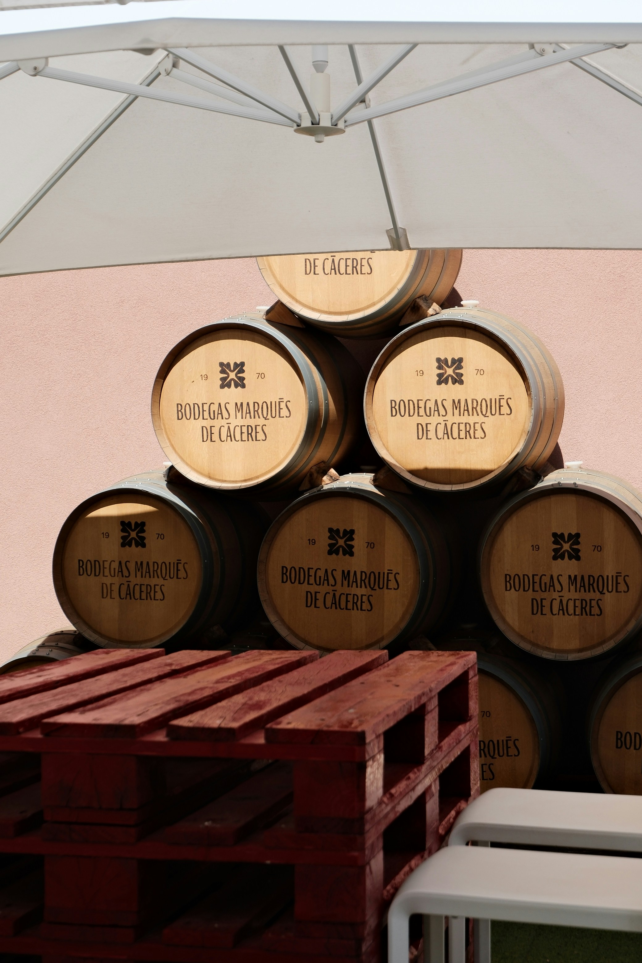 Barriles de vino de madera apilados bajo un paraguas blanco.