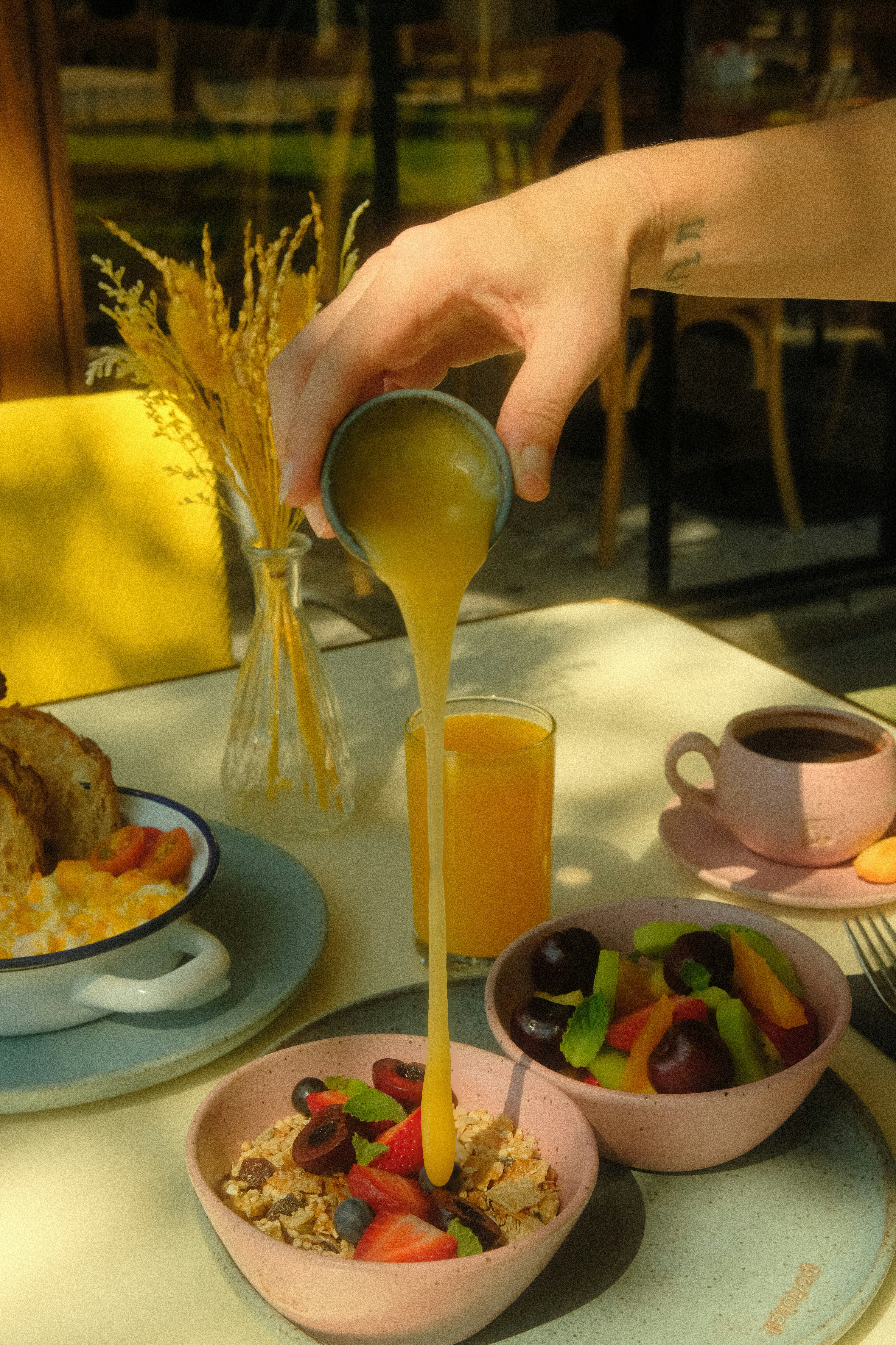 Hand pouring sauce over cereal with fruit and coffee.