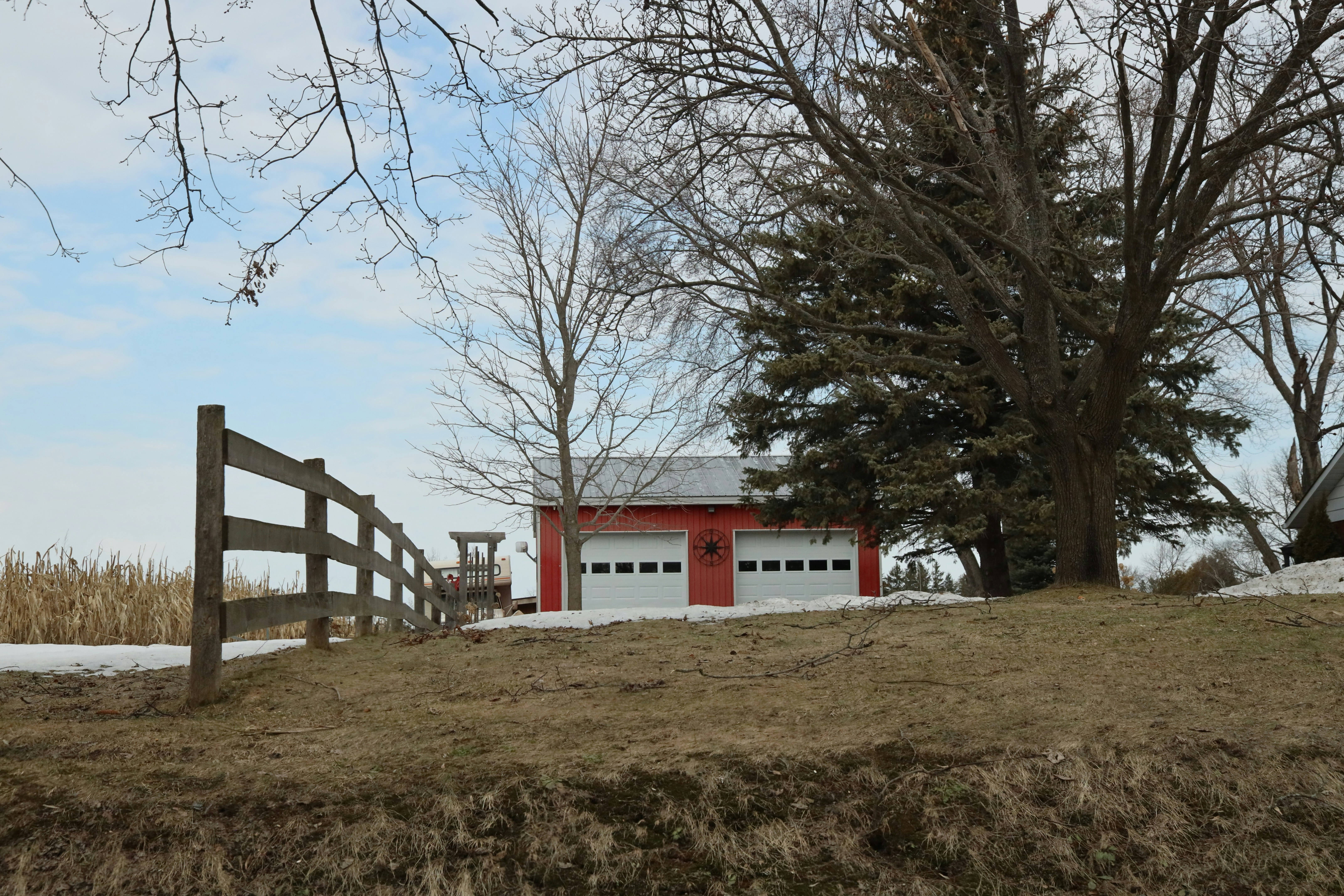 Grange rouge avec doubles portes de garage et clôture en bois.