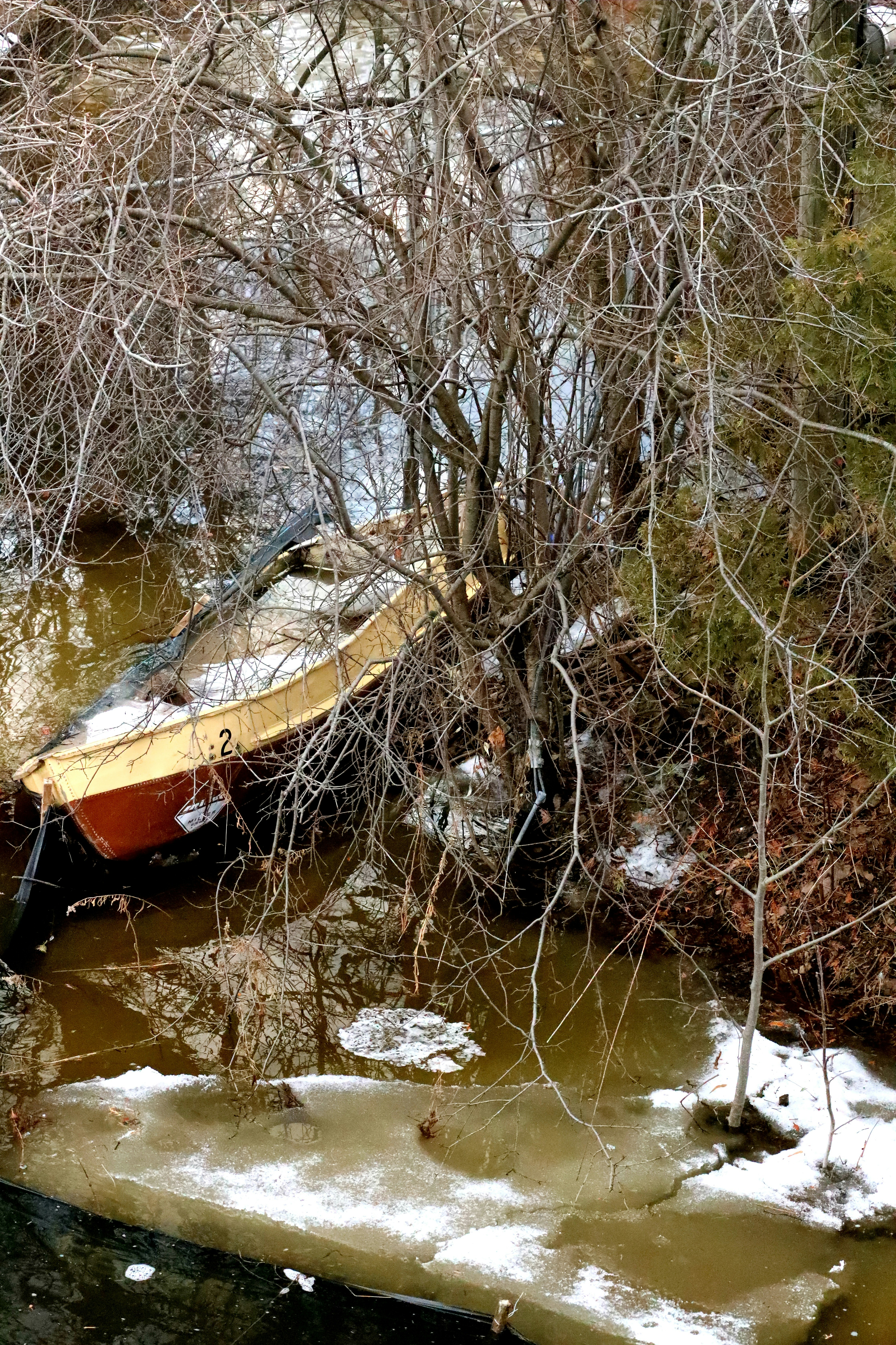 Un bateau repose dans un cours d’eau partiellement gelé et boisé.