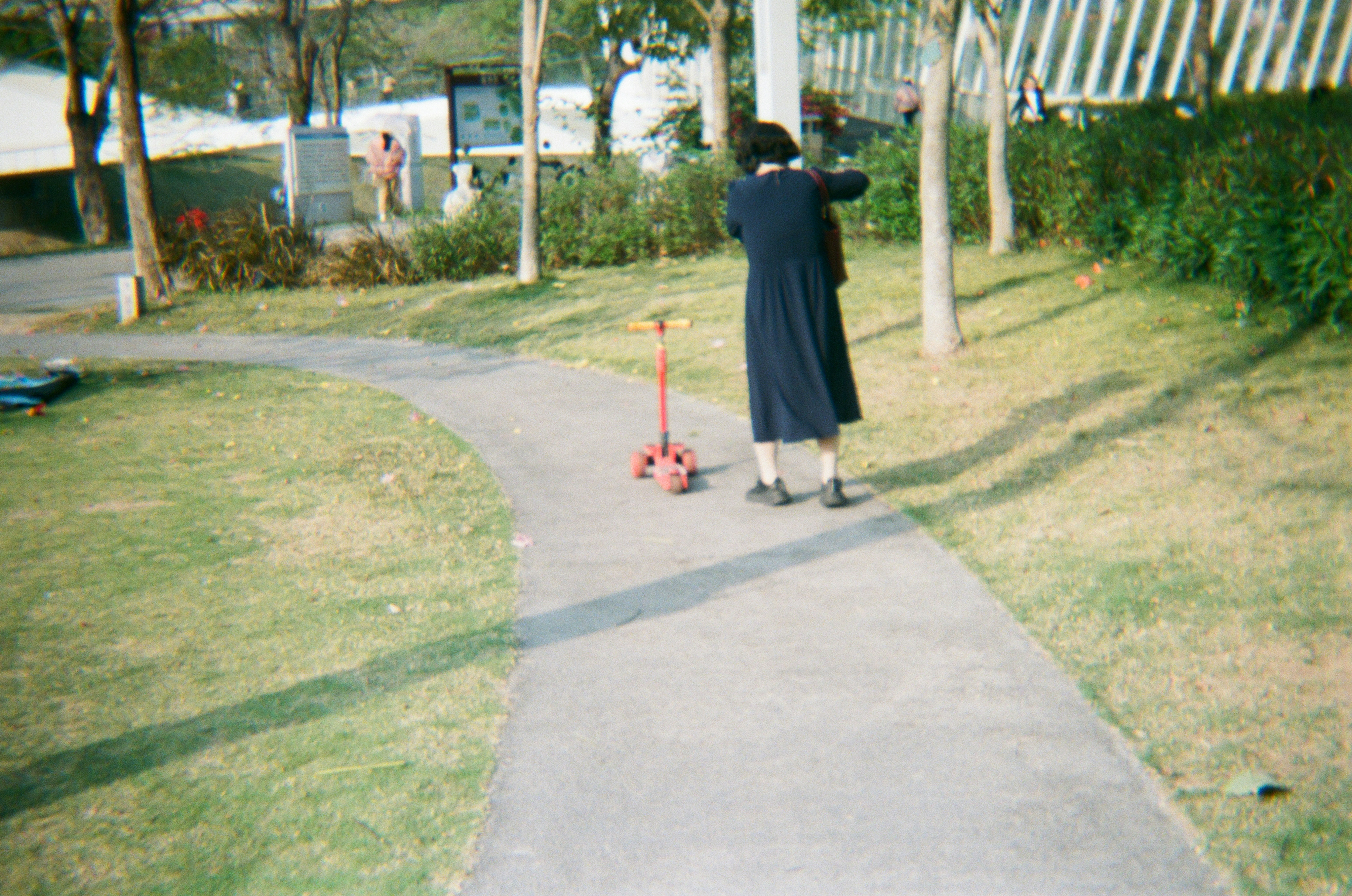 Persona con abrigo oscuro y scooter en el camino del parque