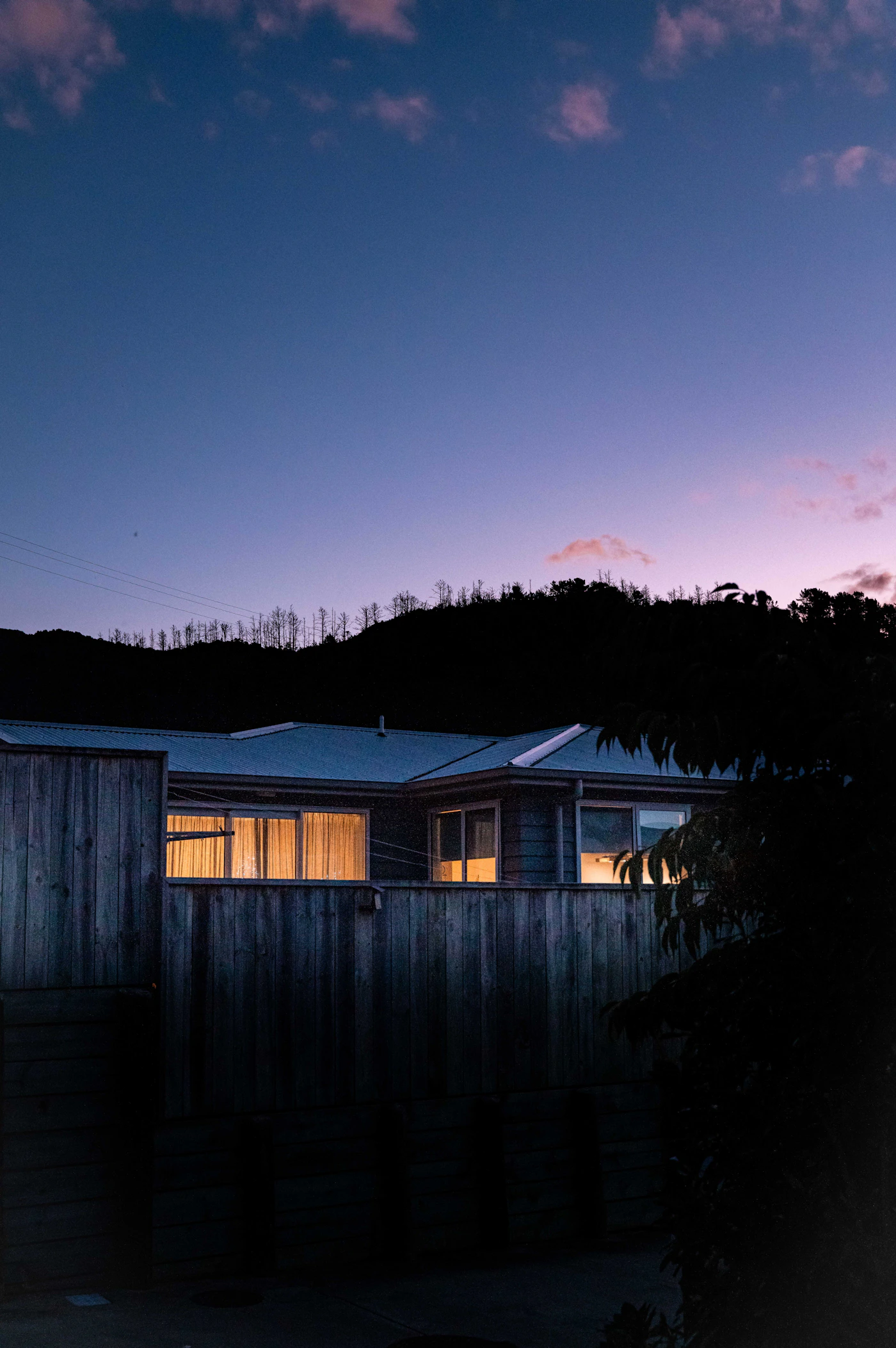 Modern residence glowing softly behind a timber garden fence at dusk