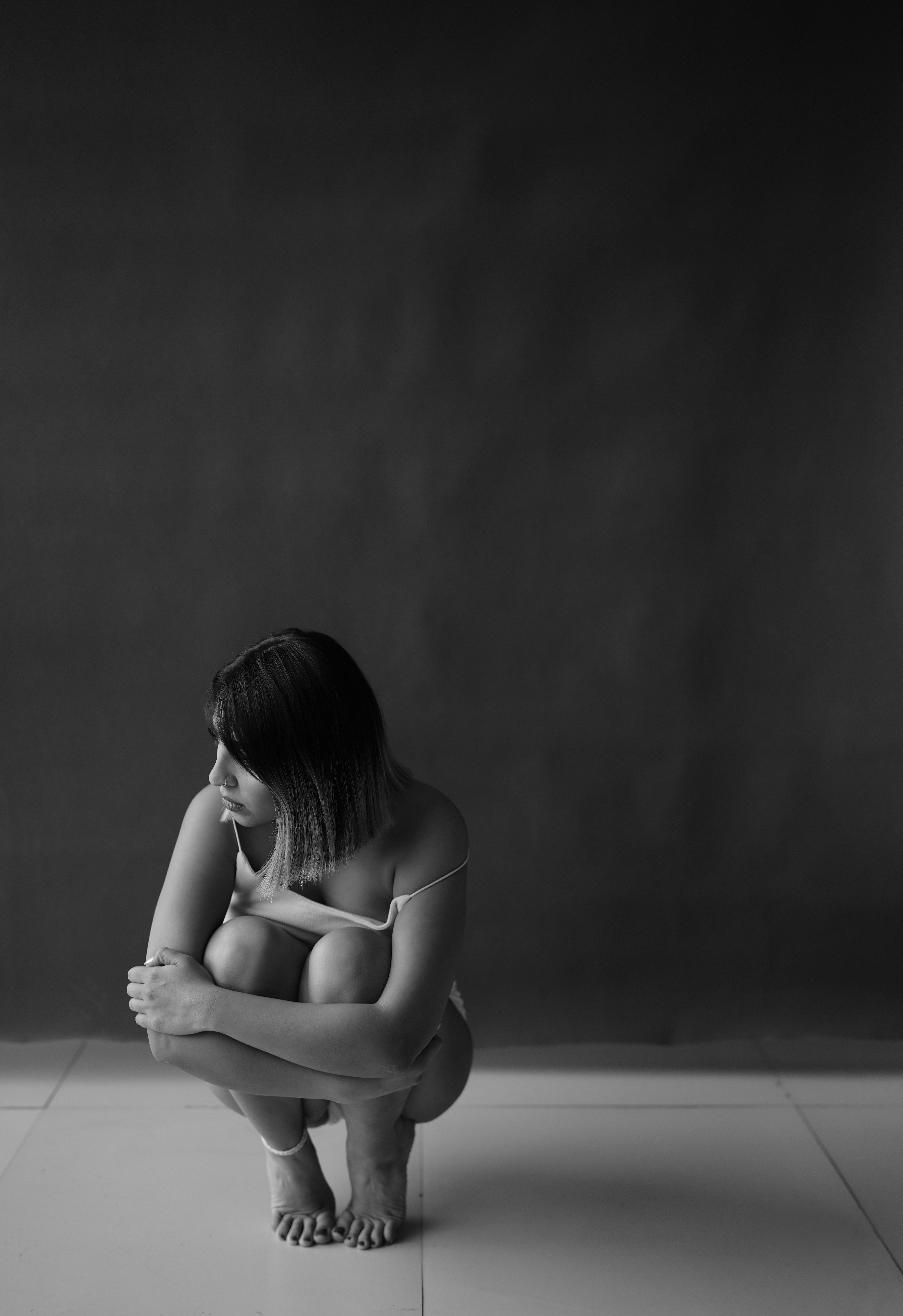 Femme accroupie, les bras autour des genoux, regardant ailleurs