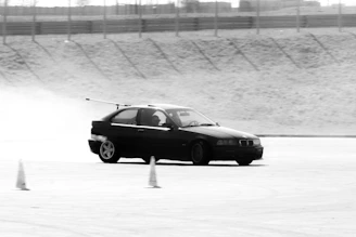 Black car drifting around cones on track