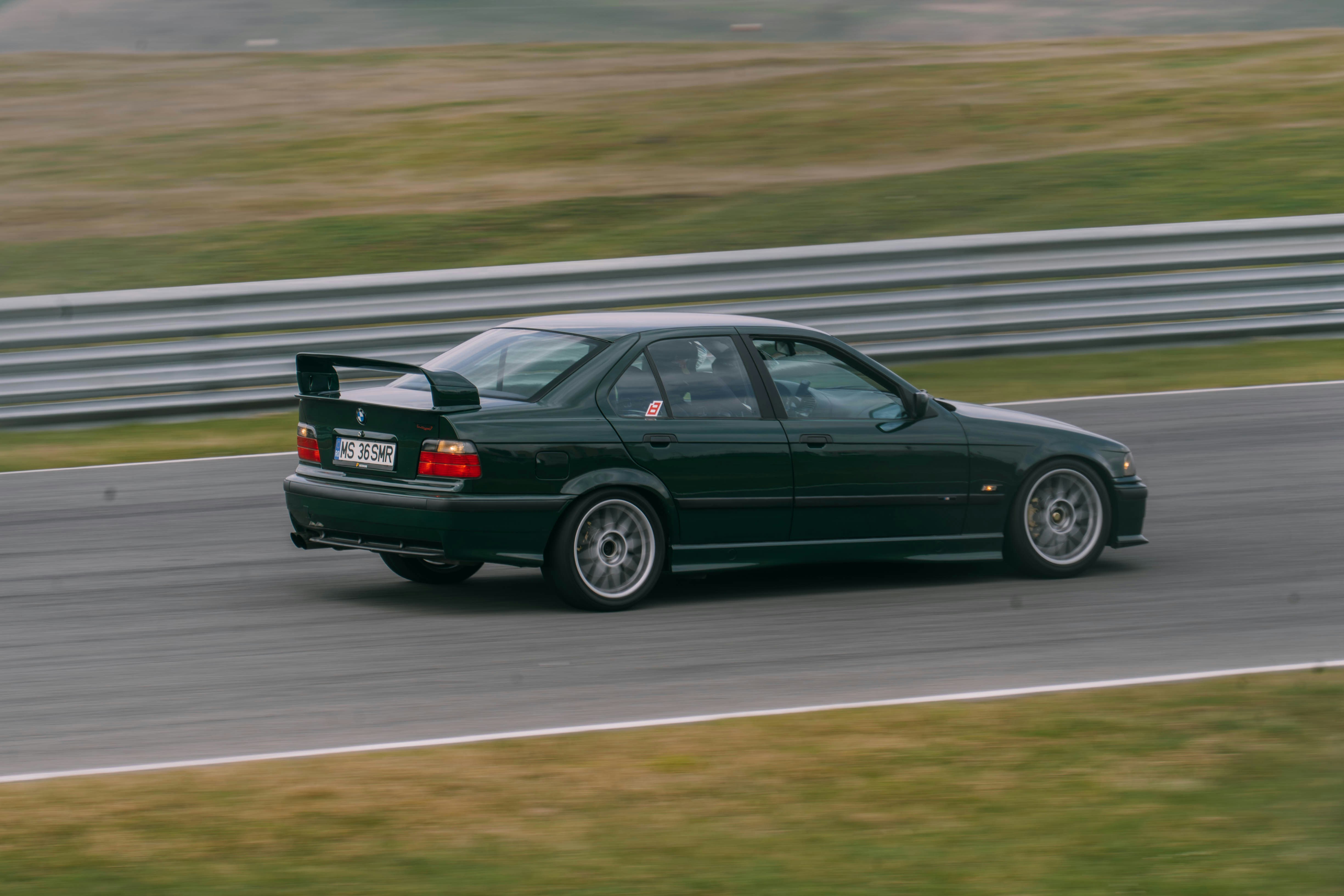 Dark green sedan with a large rear spoiler on track.