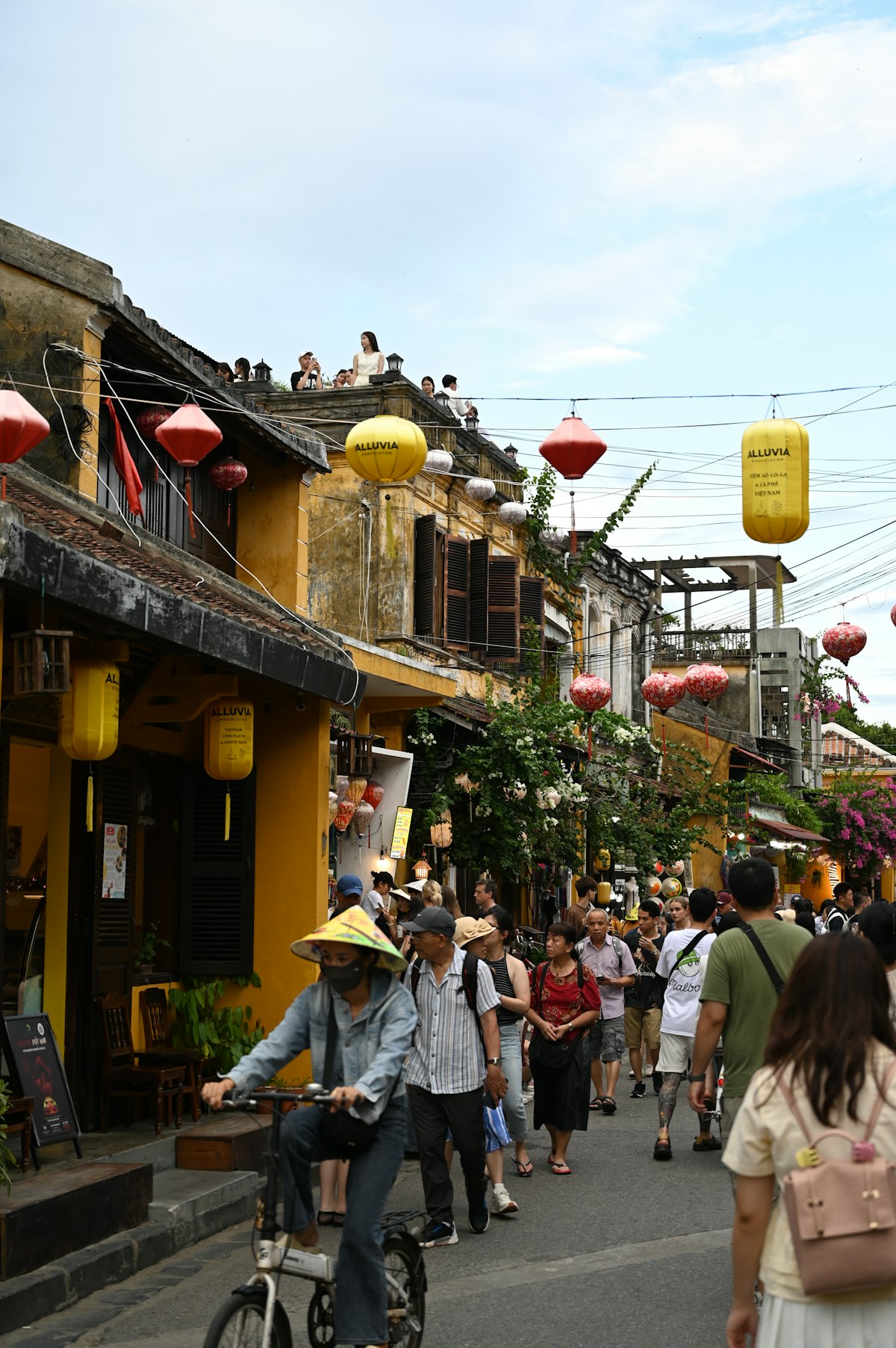 Hoi An May — pedestrians strolling a lantern-lined Ancient Town street as afternoon warmth builds