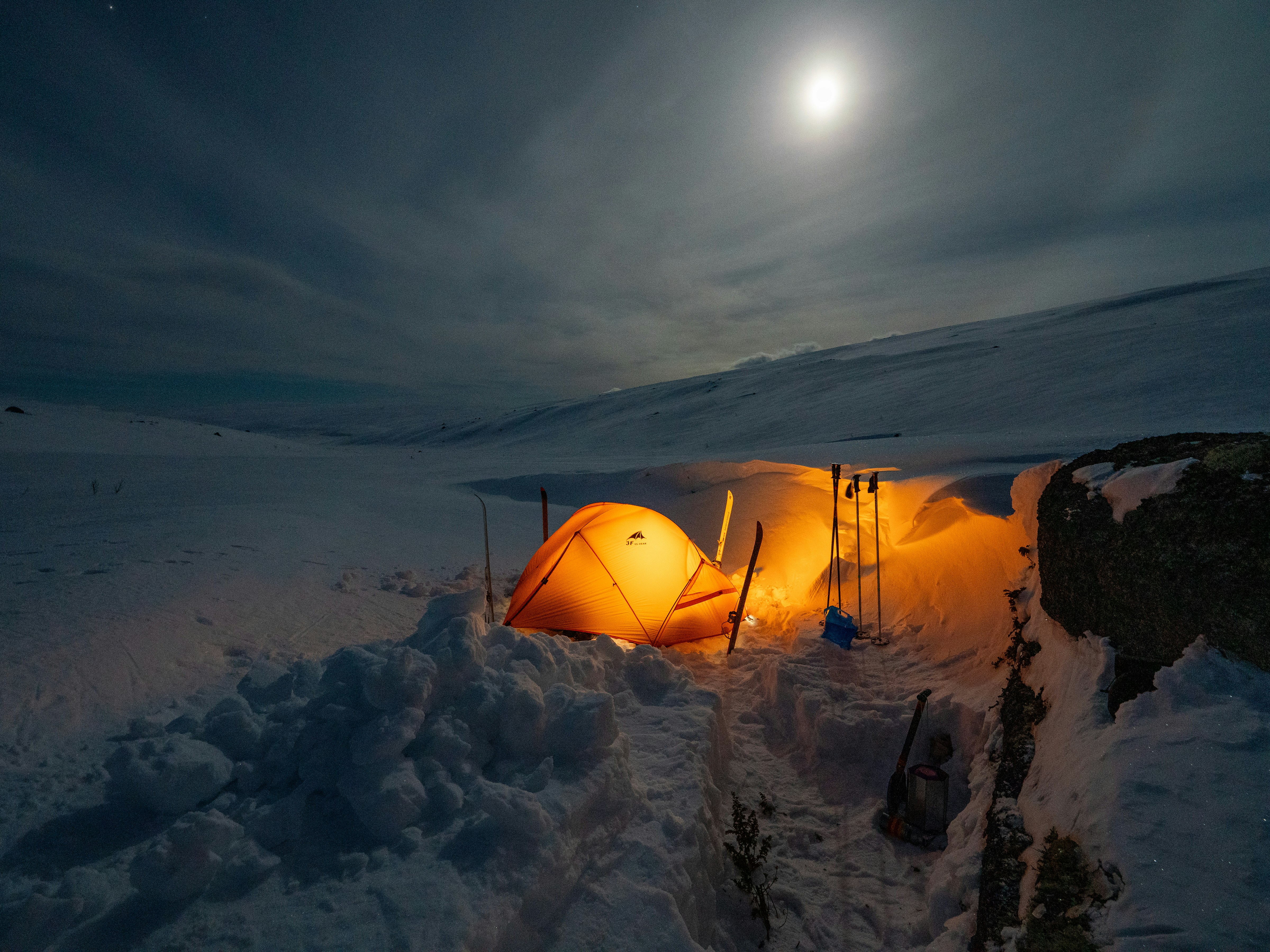 Illuminated tent in a snowy landscape under moonlight