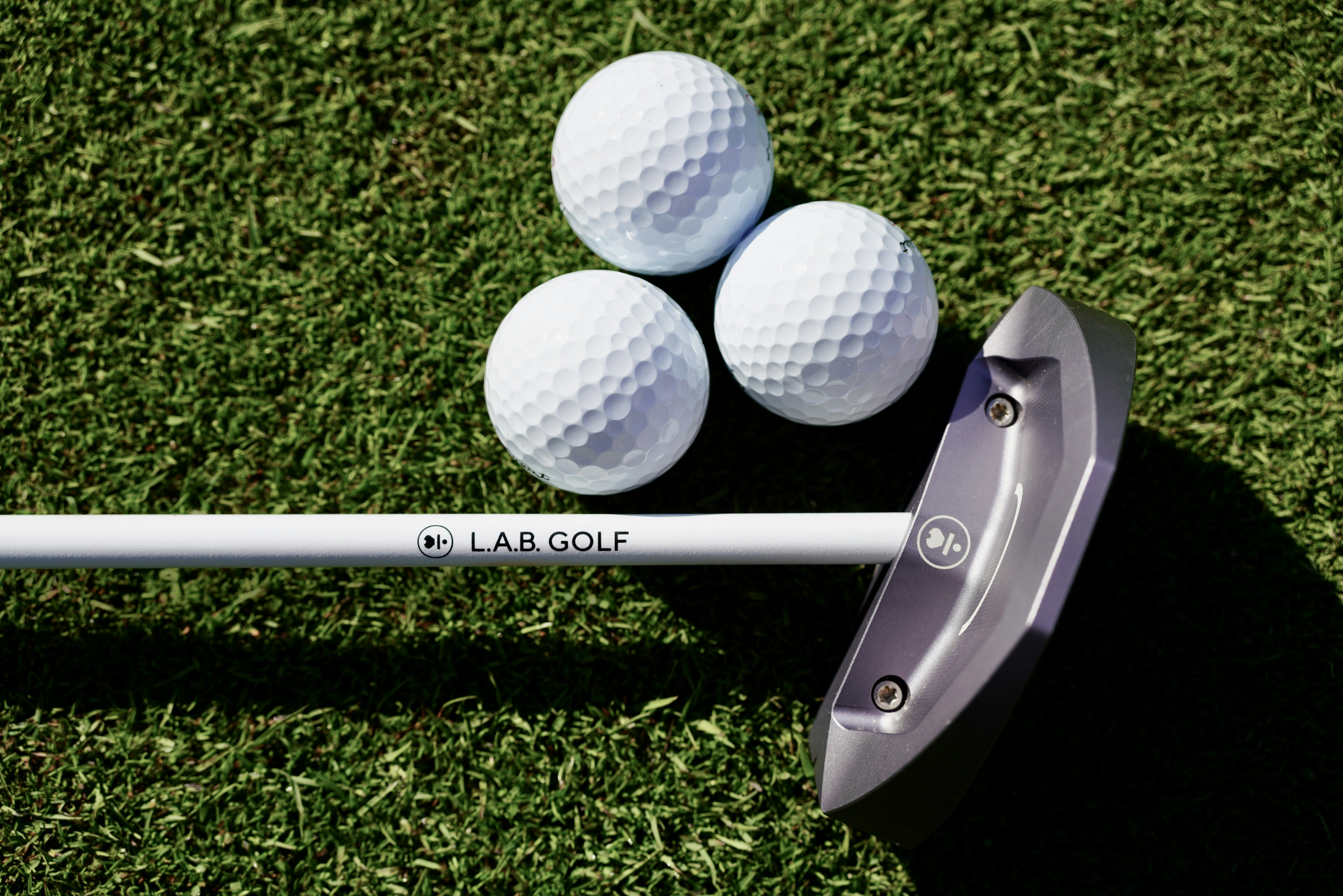 Golf putter and three balls on green grass