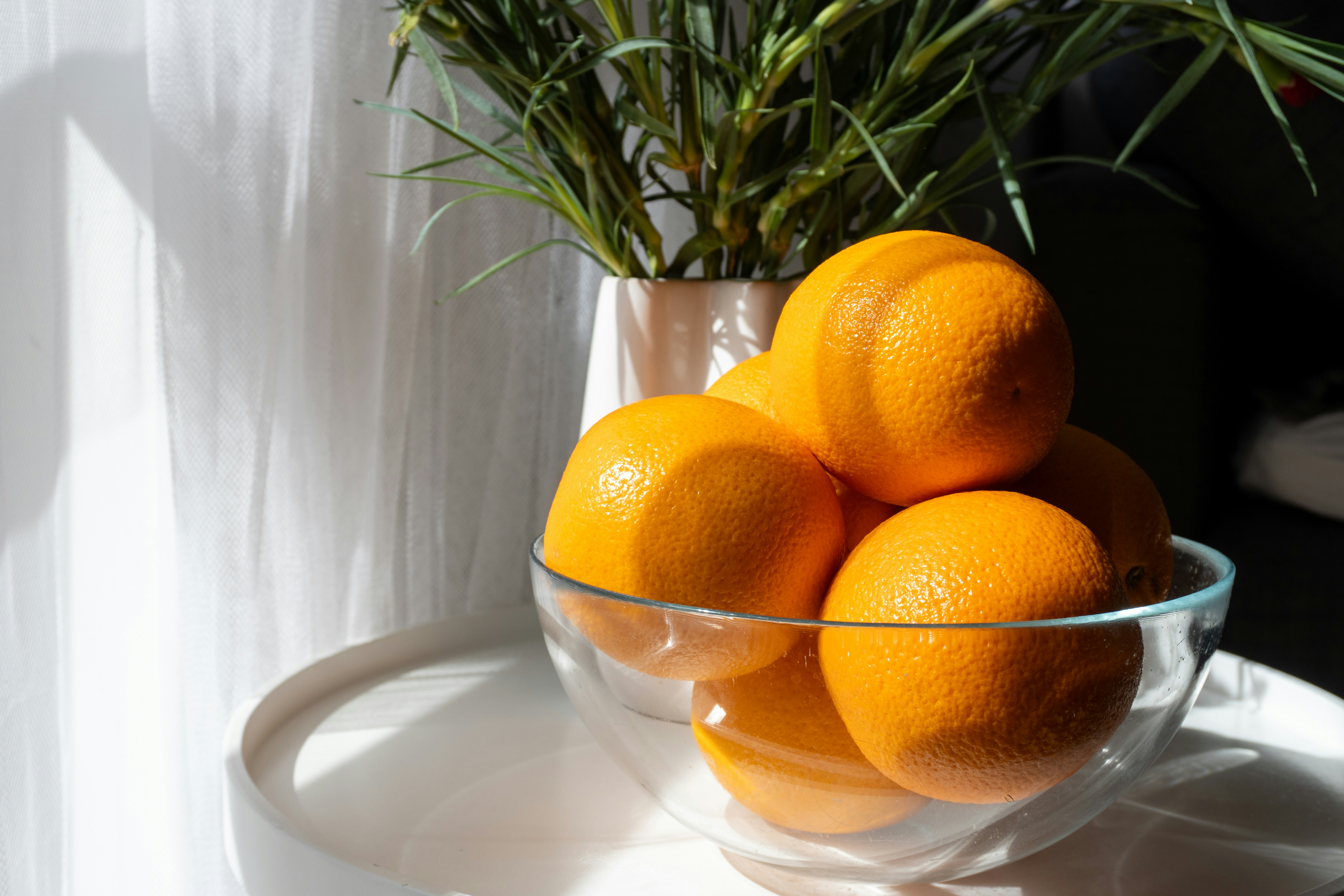 Oranges in a glass bowl with a plant