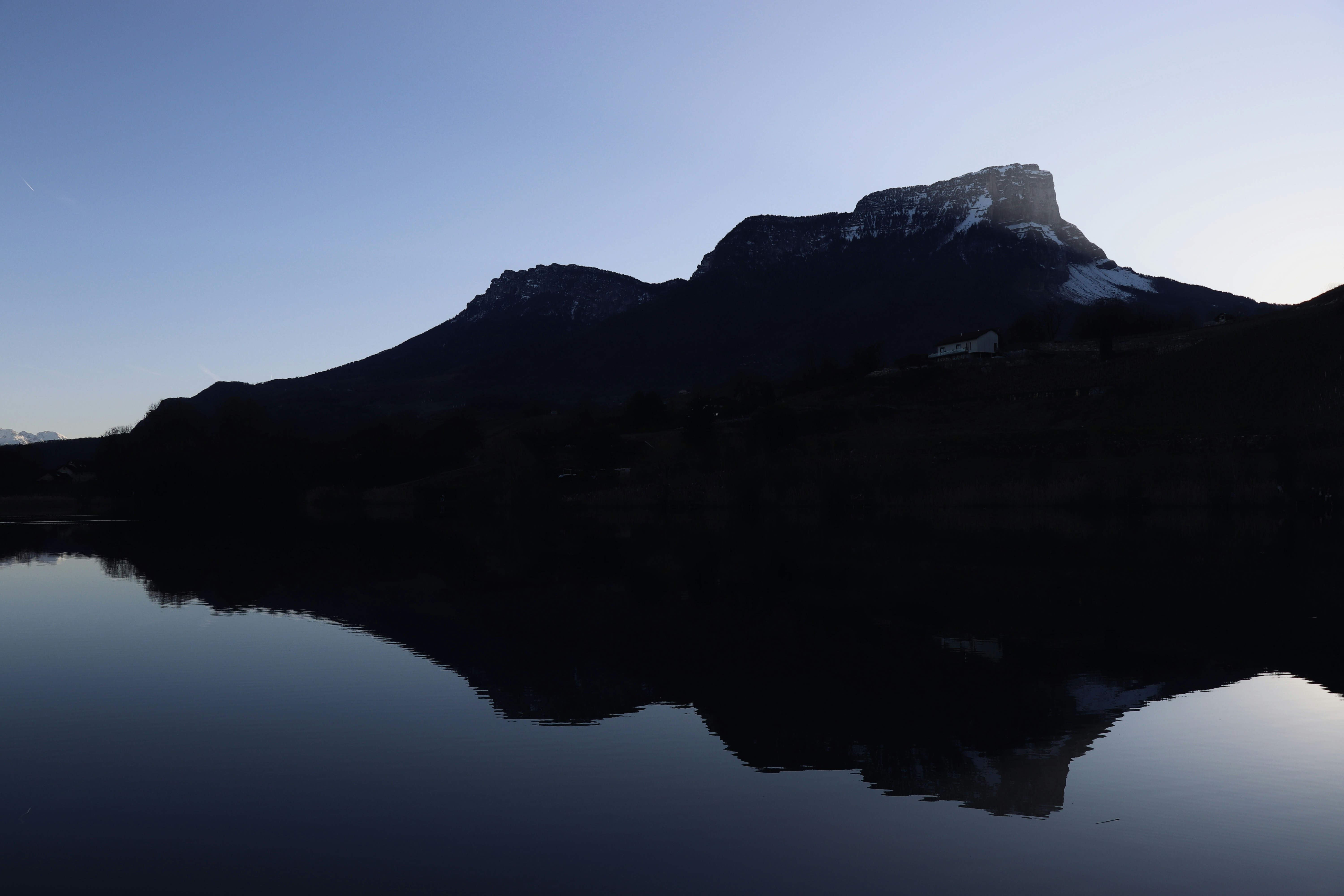 Silhouetted mountains reflected in a calm lake at dawn.