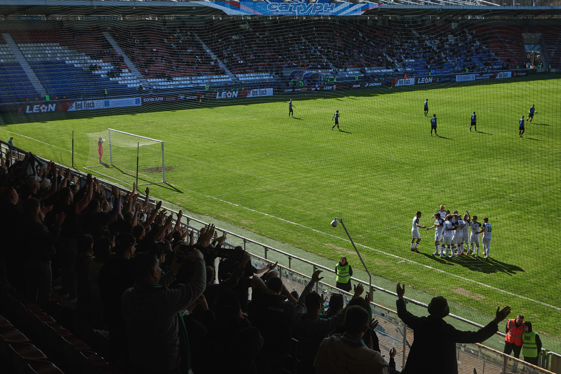 Soccer players celebrate on a grassy field with cheering fans.
