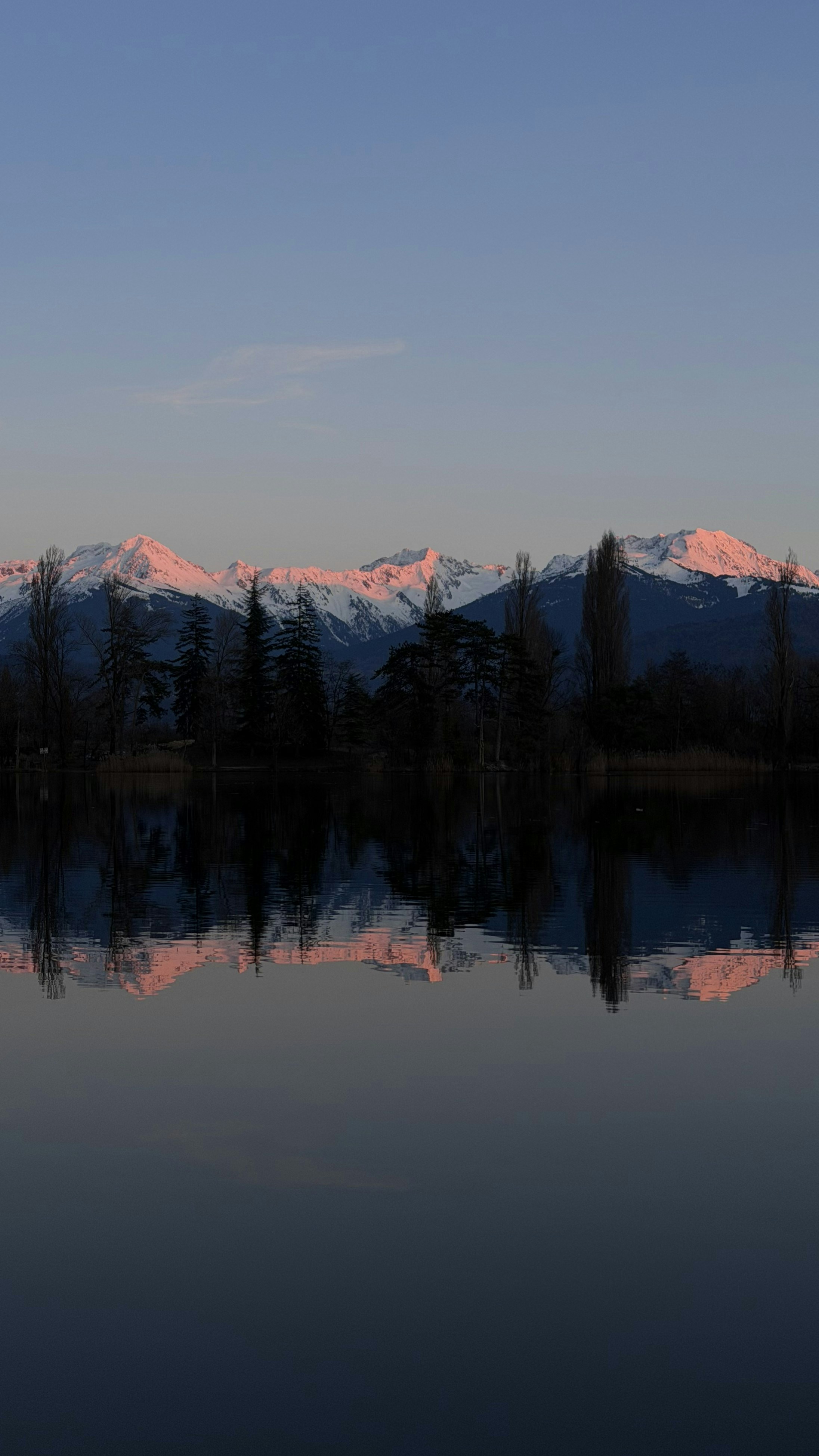 Snow-capped mountains reflected in still water at sunset.