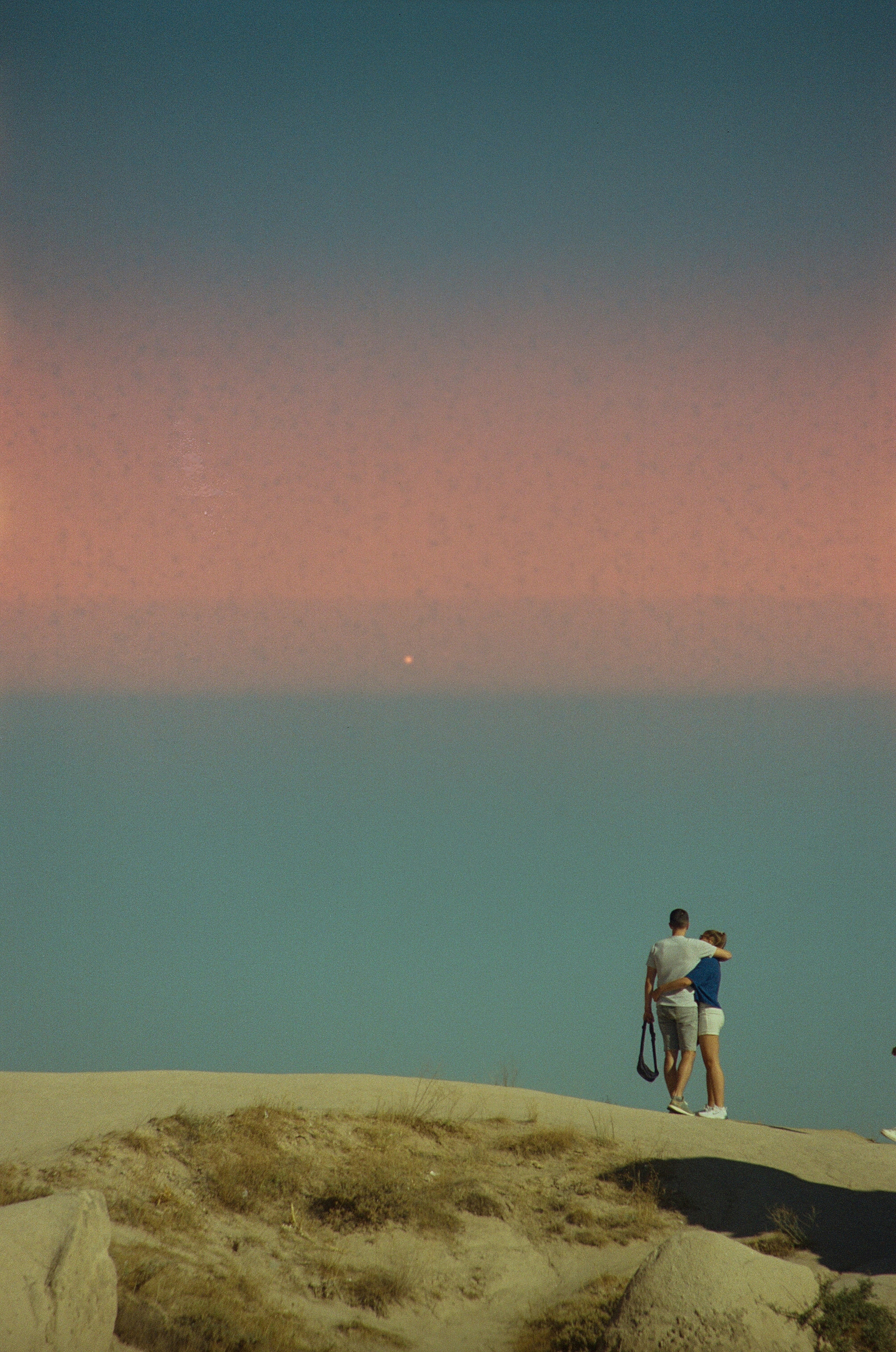 Pareja abrazada en un acantilado con vistas al océano al atardecer