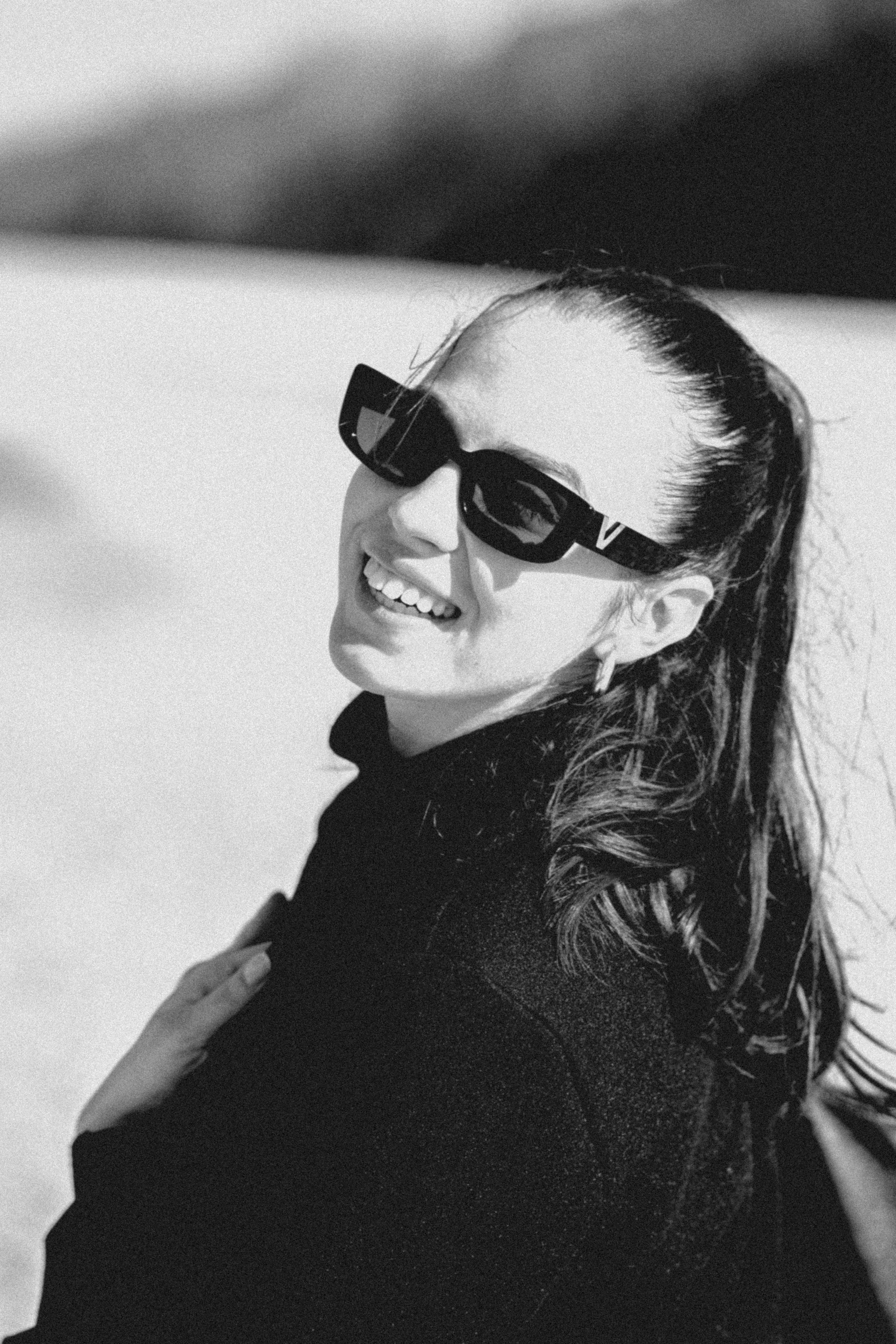 Seorang wanita tersenyum mengenakan kacamata hitam dan sweter hitam.