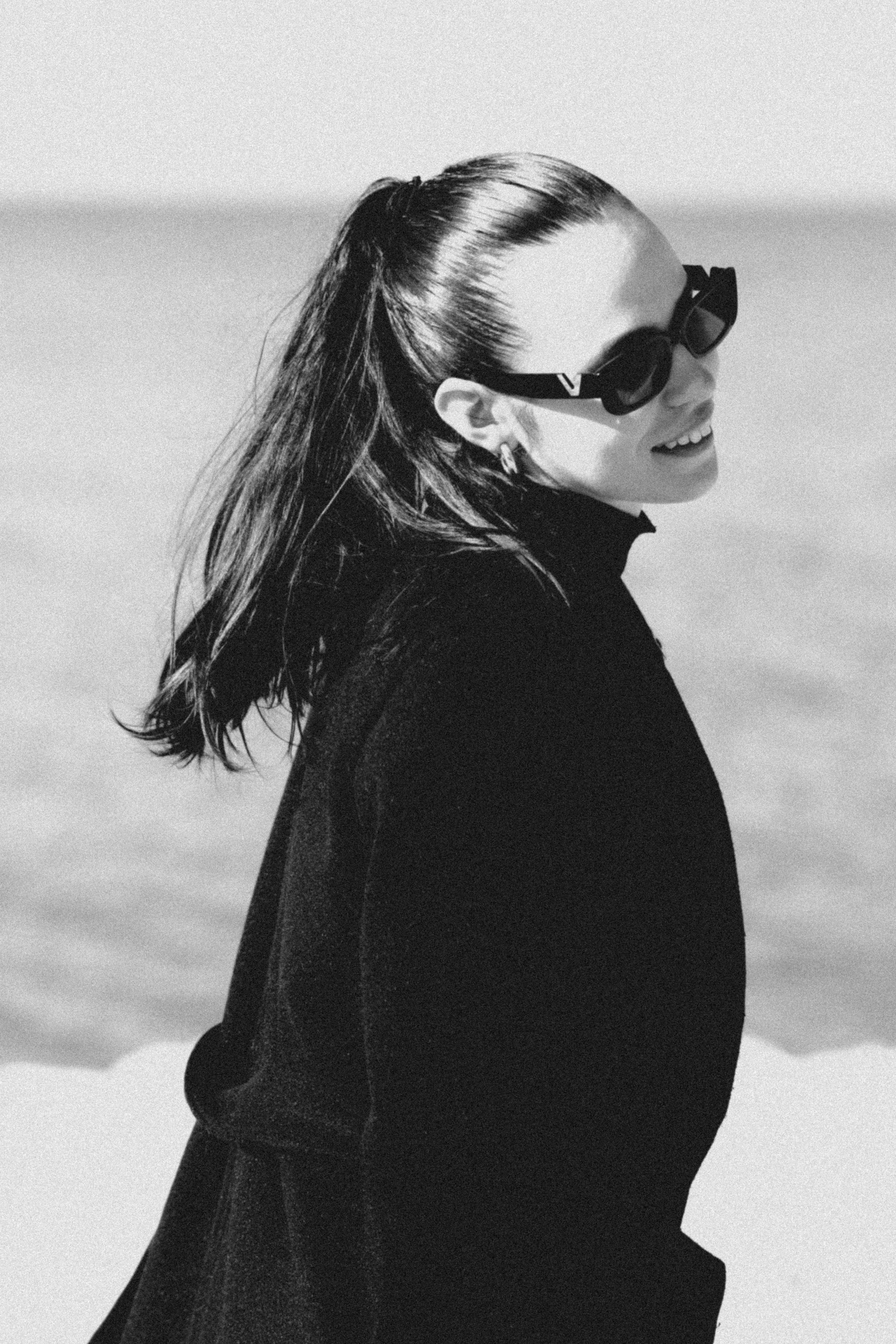 Wanita berkacamata hitam dan mantel hitam di tepi air