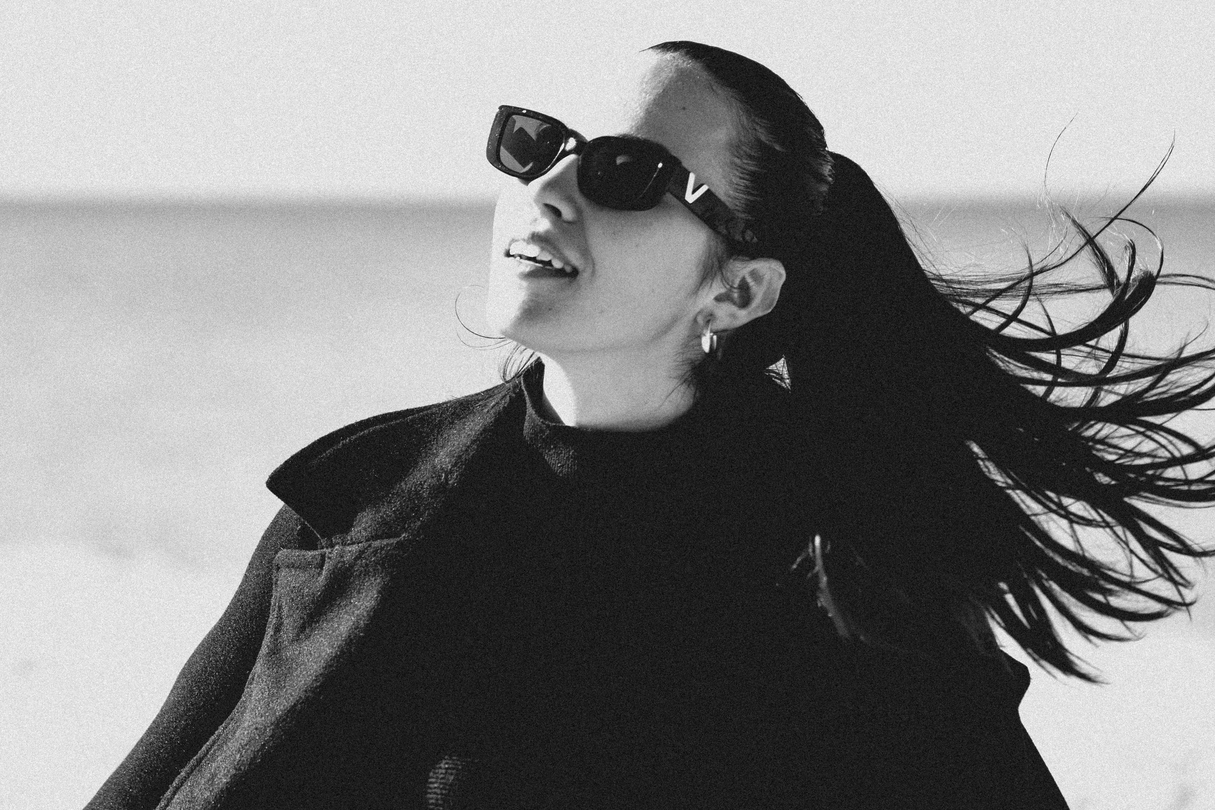 Wanita dengan kacamata hitam dan rambut tertiup angin di pantai